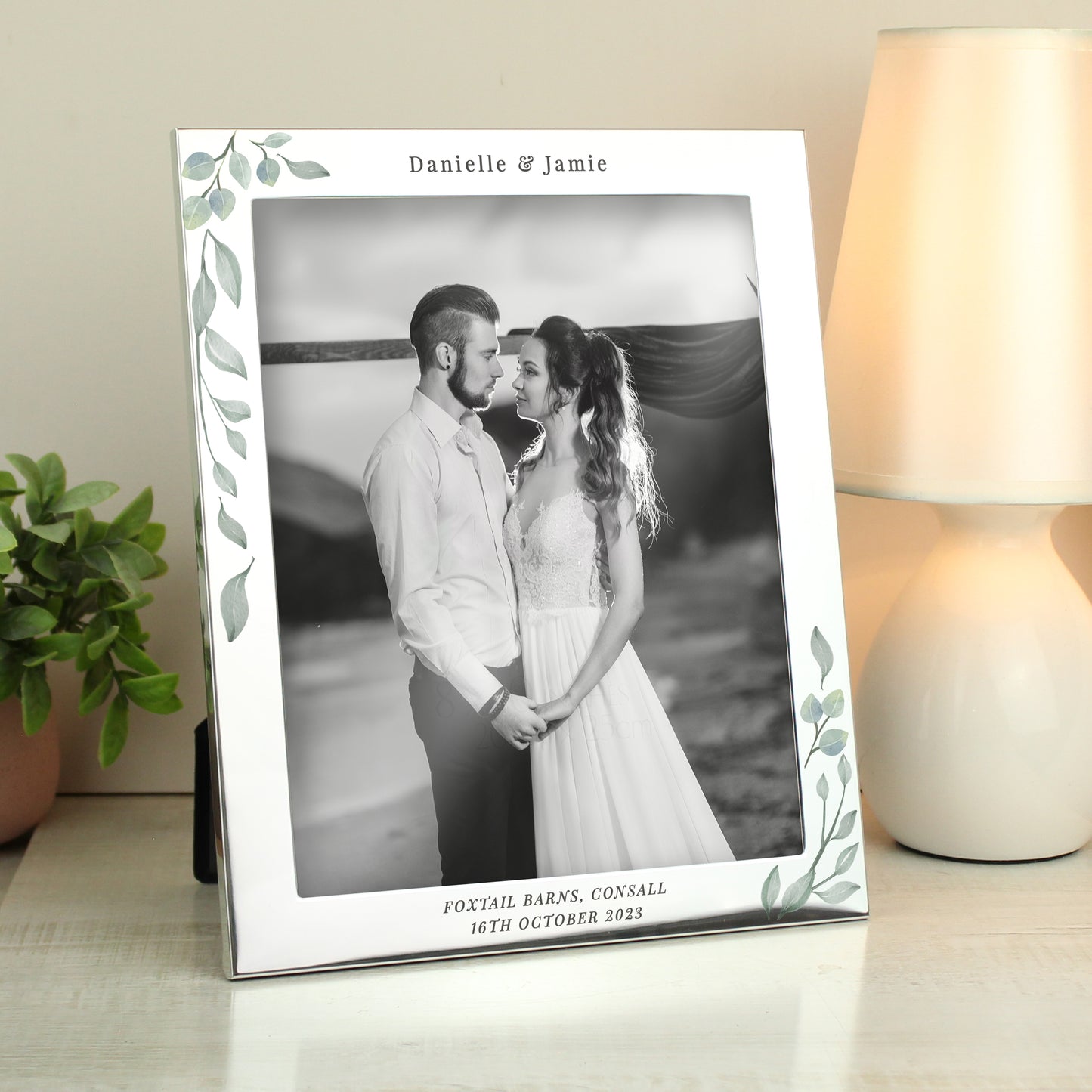 Silver frame with leaf decoration showing wedding photo. Personalised with Danielle & Jamie above the photo and Foxtail Barns, Cornwall 16th October 2023 below it.