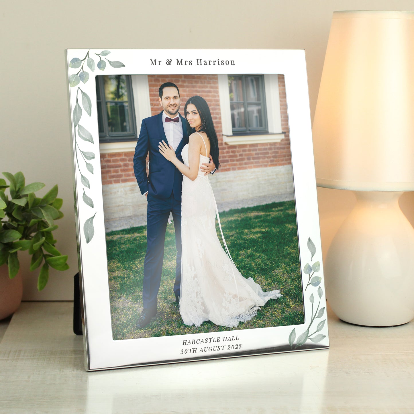 Silver frame with leaf decoration showing wedding photo. Personalised with Mr & Mrs Harrison above the photo and Harcastle Hall 30th August 2023 below it.