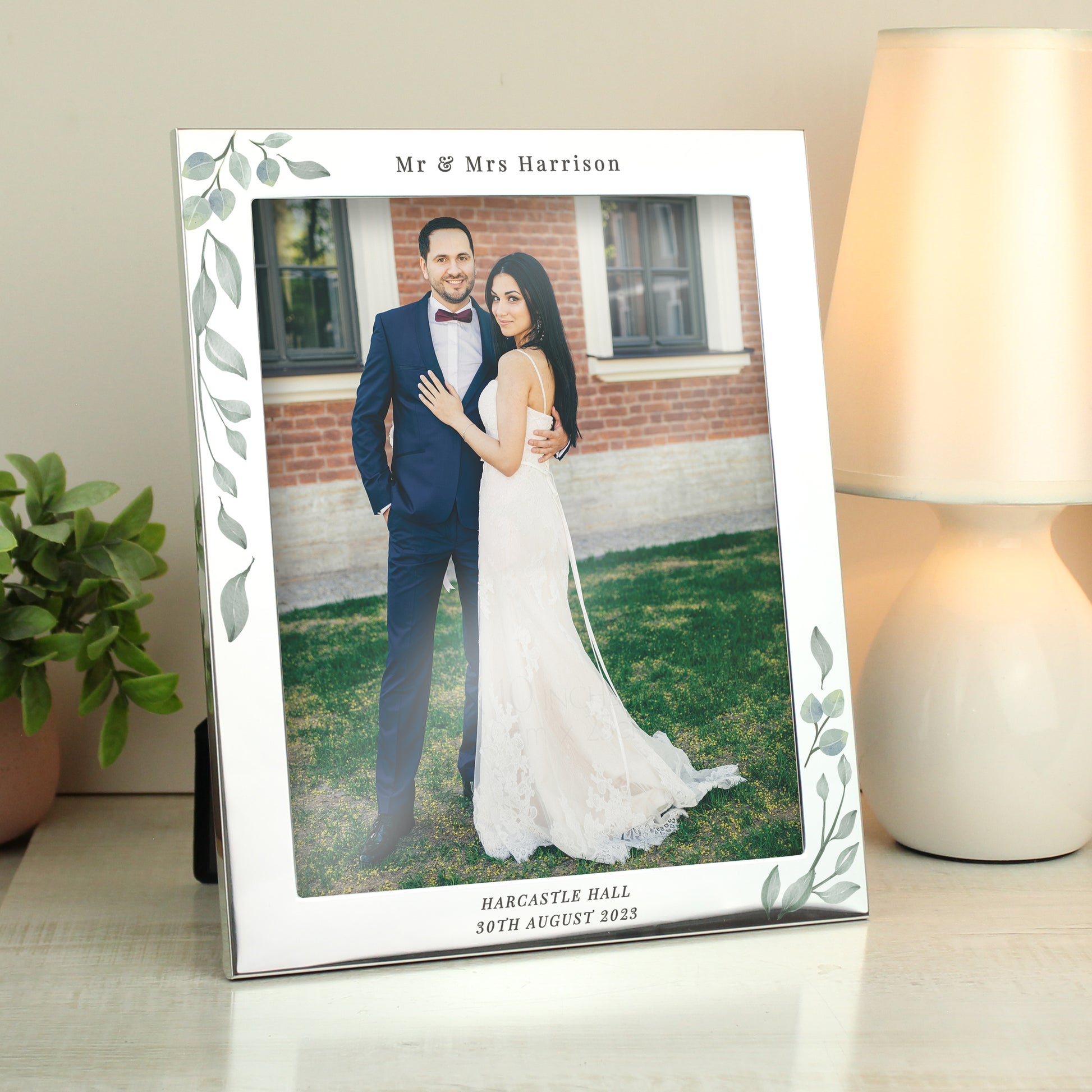 Silver frame with leaf decoration showing wedding photo. Personalised with Mr & Mrs Harrison above the photo and Harcastle Hall 30th August 2023 below it.