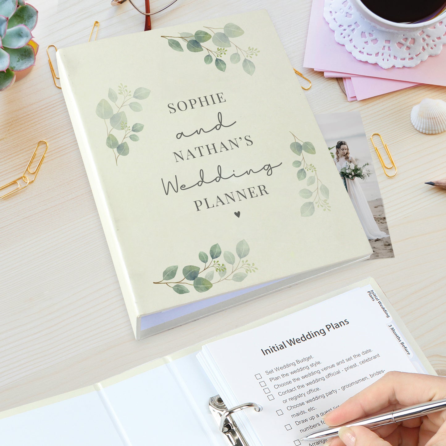 Wedding planner book with 'Sophie and Nathan's Wedding Planner' on a desk with stationery items.