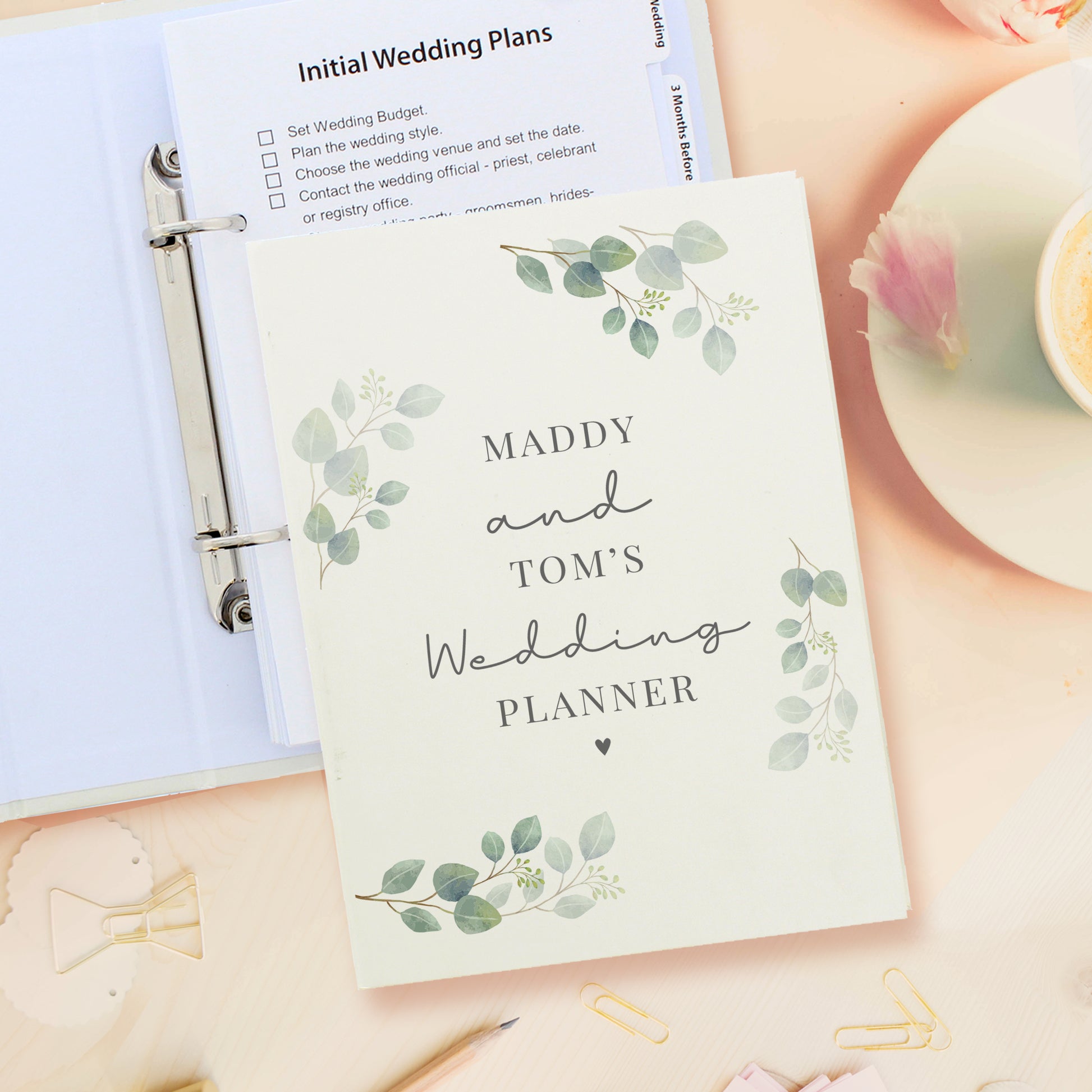 Wedding planner book with 'Maddy and Tom's Wedding Planner' on a desk with stationery items.