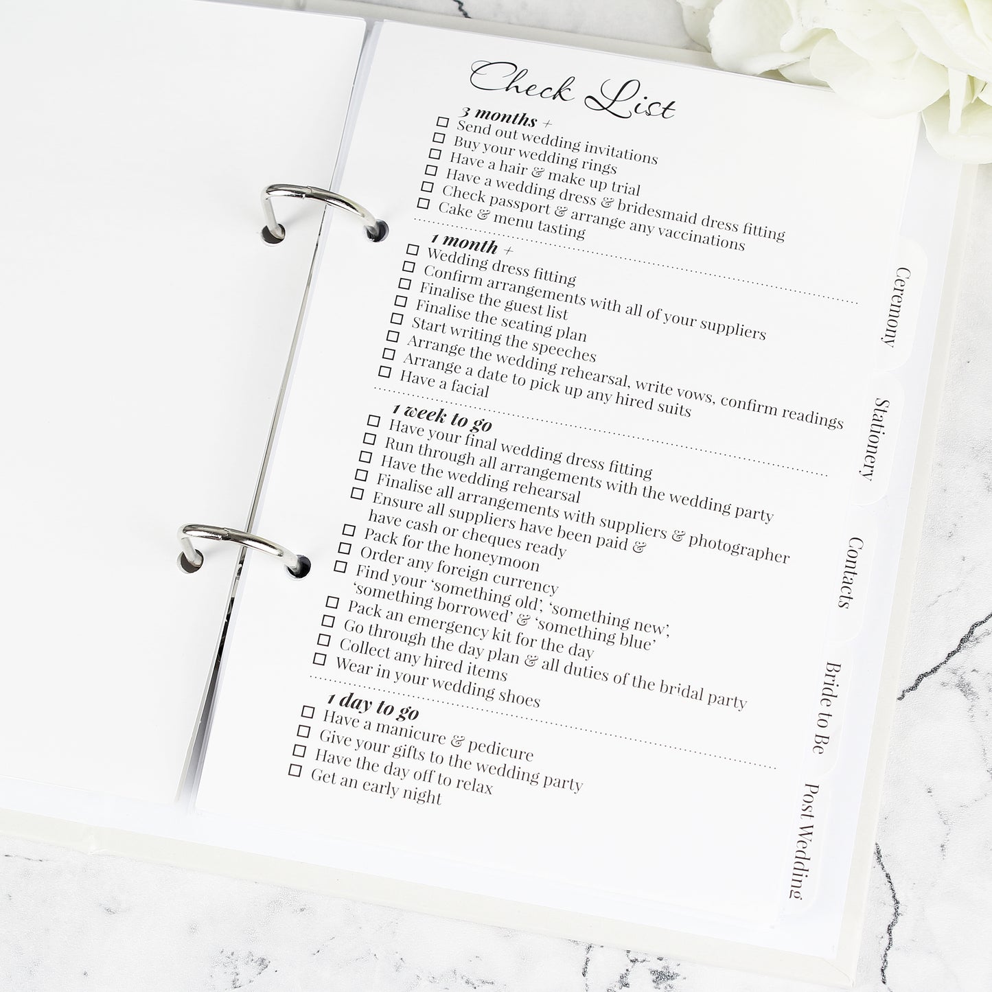 Checklist for wedding preparation on a marble surface with white flowers.