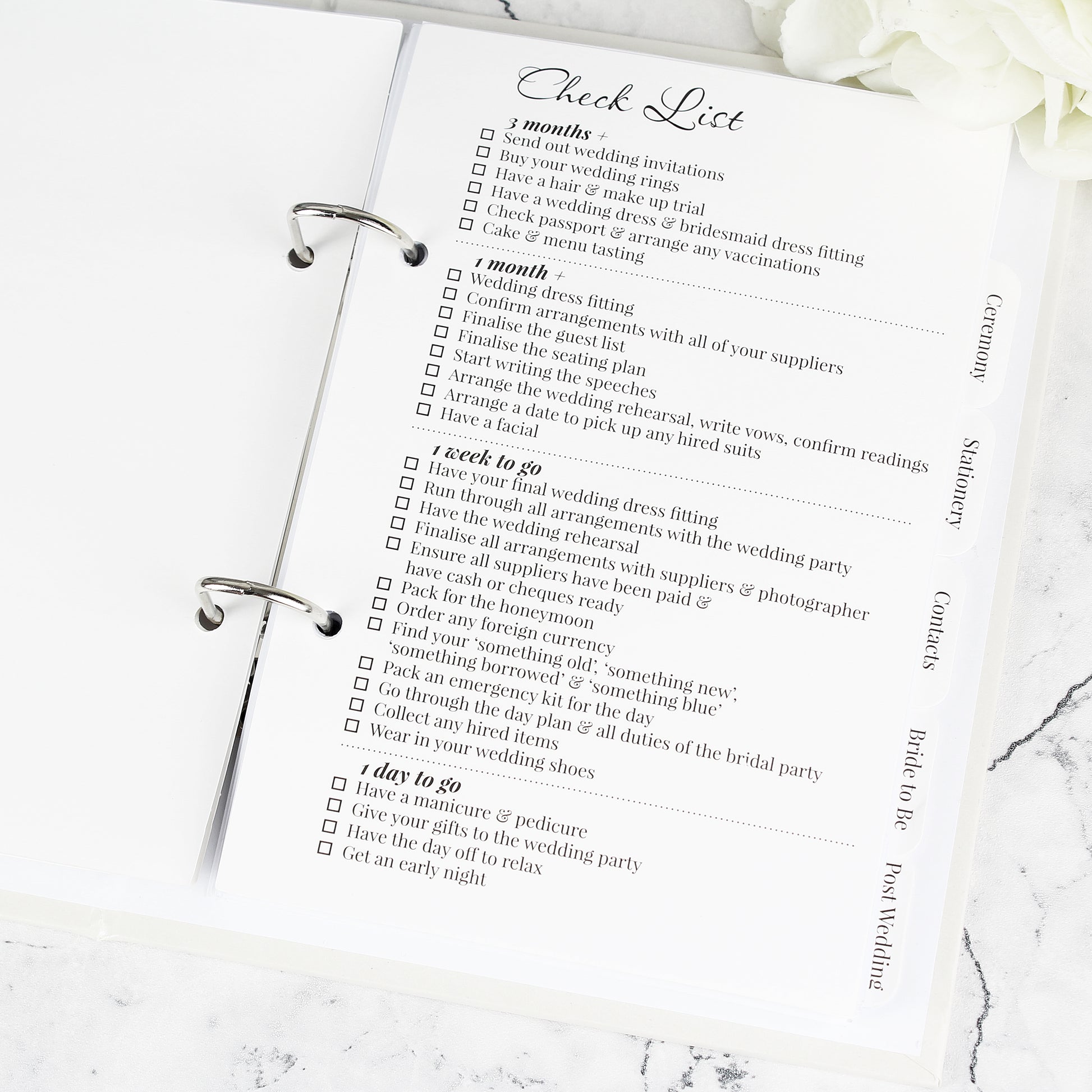 Checklist for wedding preparation on a marble surface with white flowers.