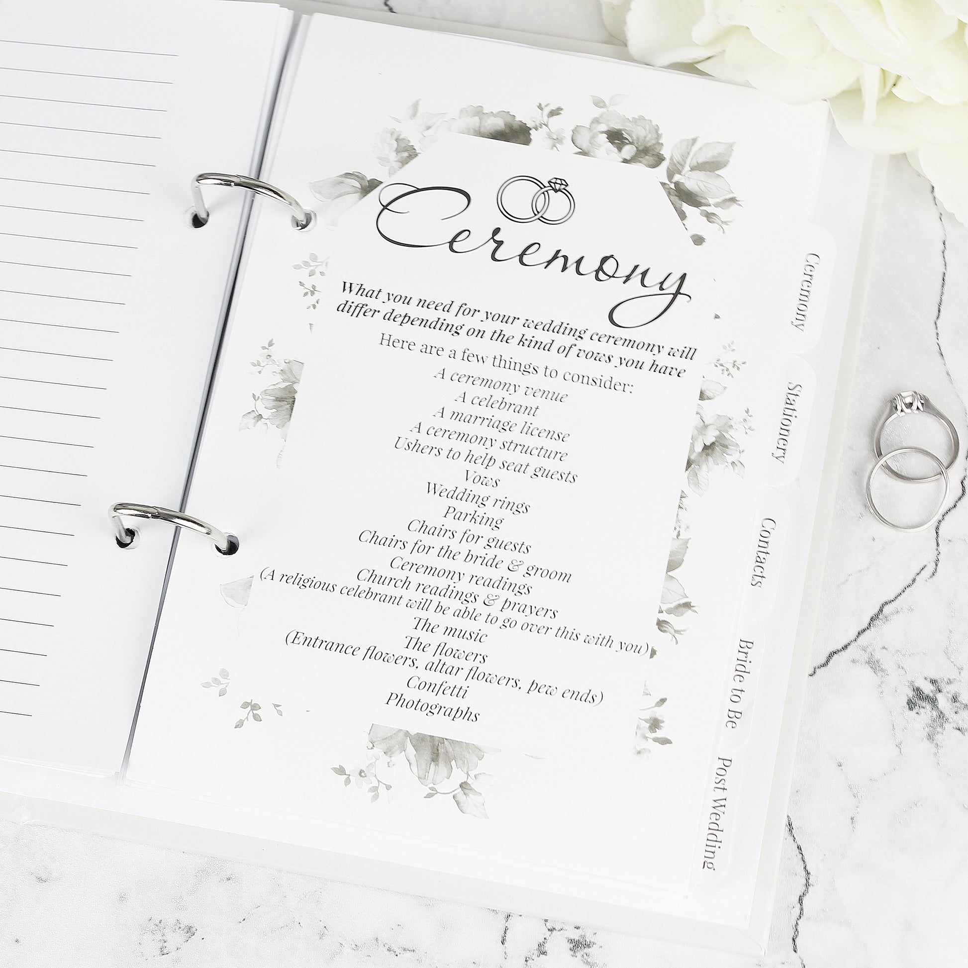 Wedding planner book with 'Ceremony' section and wedding rings on a marble surface