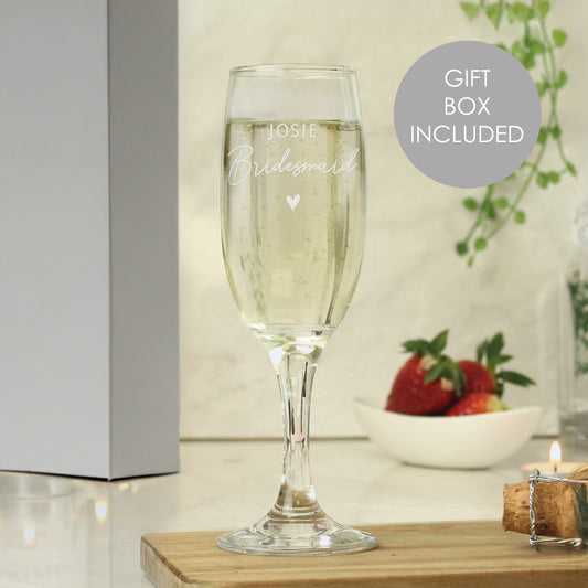 Champagne flute with engraved text on a wooden surface with a gift box and strawberries in the background.