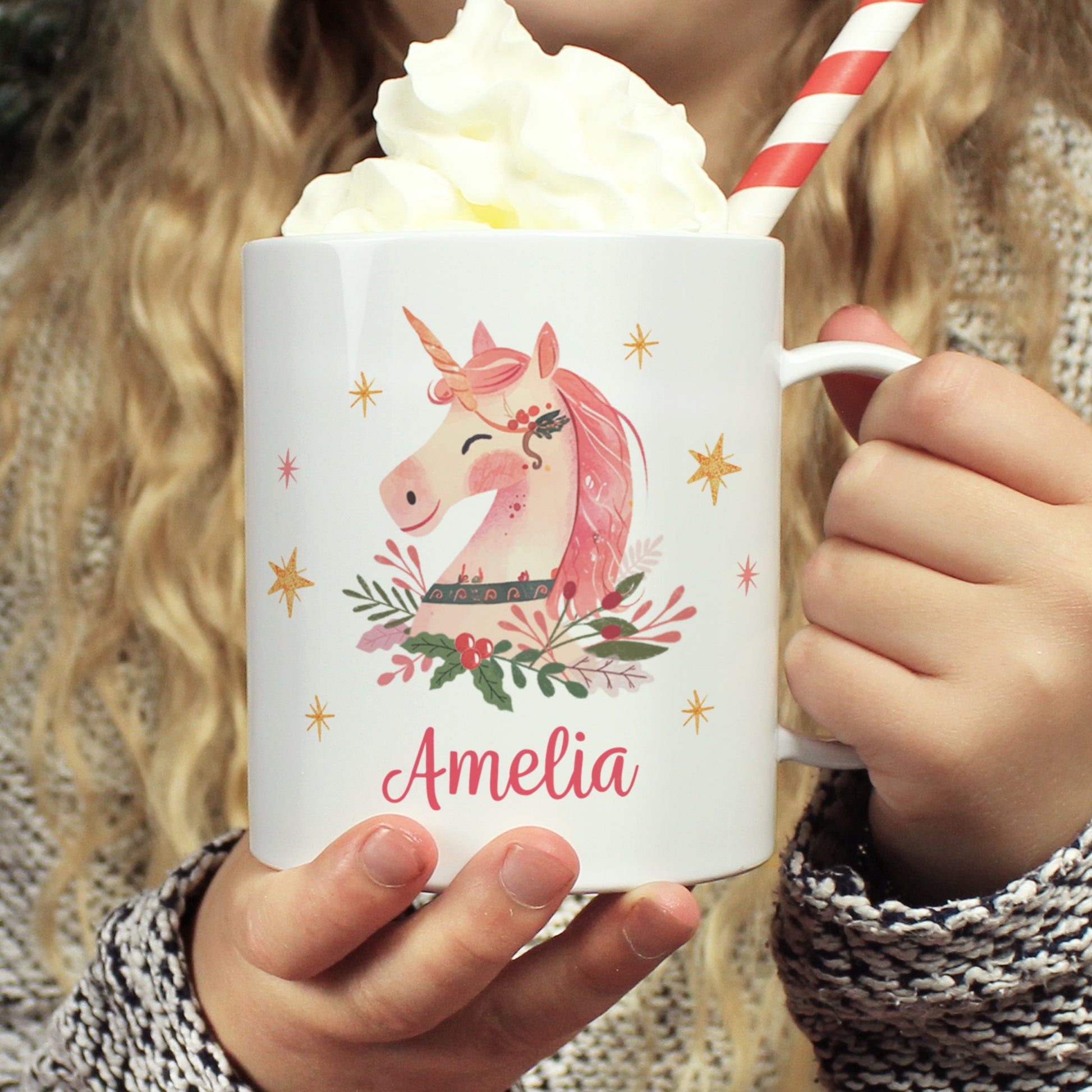 White plastic Christmas mug held by a child. Pink unicorn image and text reading Amelia.