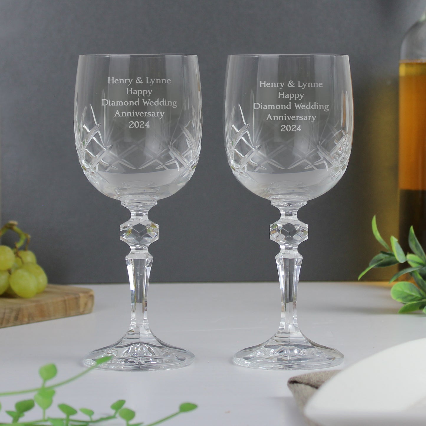 Two crystal wine glasses with engraved text on a table with a grey background.