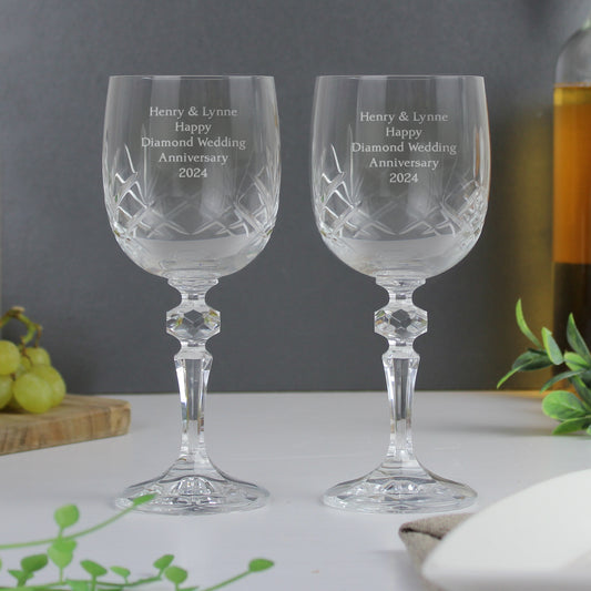 Two crystal wine glasses with engraved text on a table with a grey background.