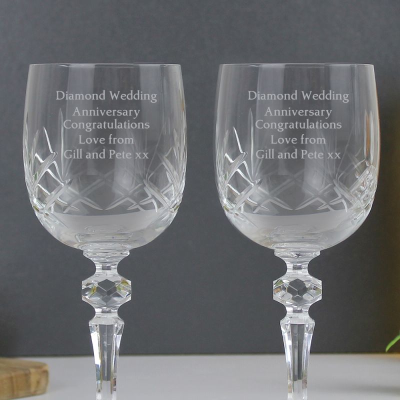 Two crystal wine glasses with engraved text on a grey background