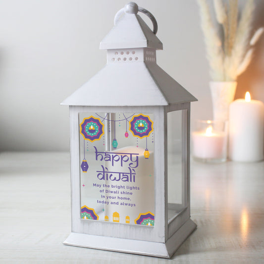 Personalised white Diwali lantern stood on a worktop with candles and bullrushes in the background.