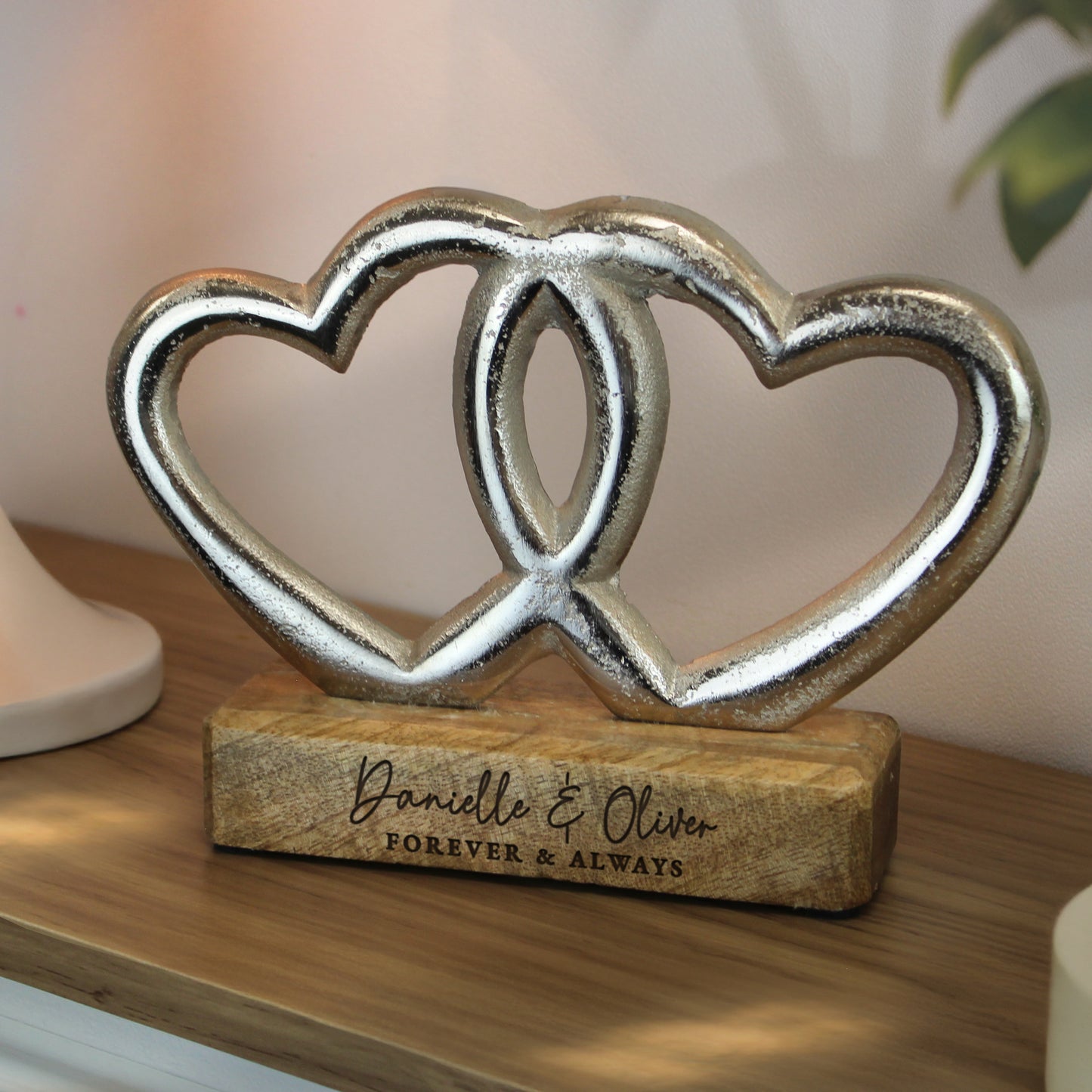 Decorative sculpture of two interlocking hearts on a wooden base with engraved text, placed on a wooden surface.
