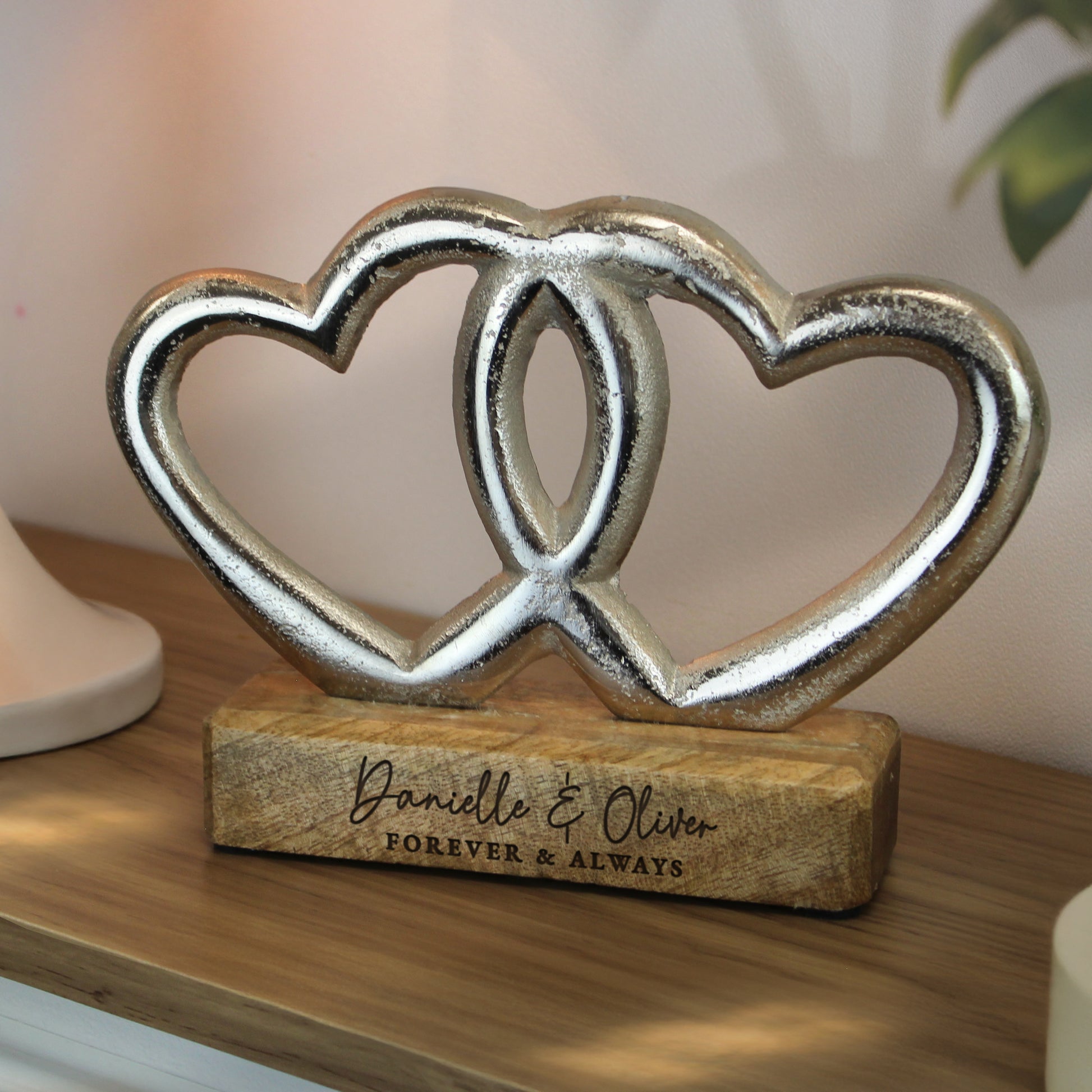 Decorative sculpture of two interlocking hearts on a wooden base with engraved text, placed on a wooden surface.