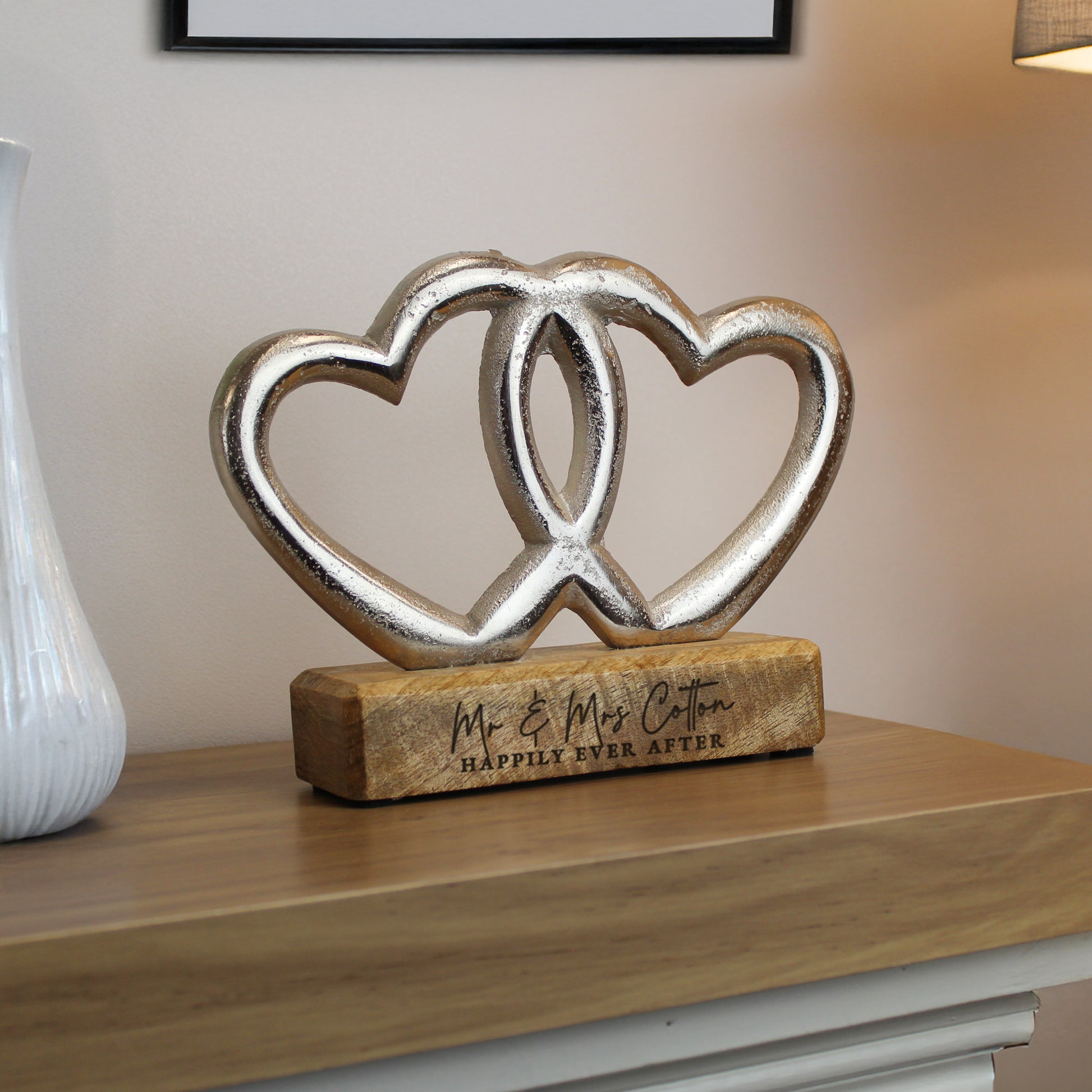 Decorative sculpture of two interlocking hearts on a wooden base with text, placed on a surface.