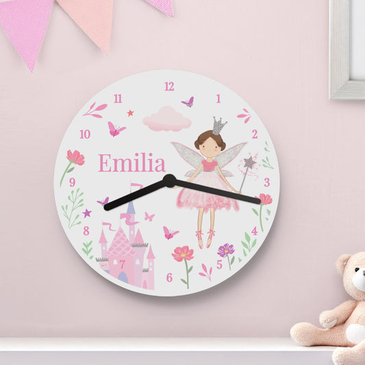 Children's wall clock with fairy design and 'Emilia' on a pink wall with a teddy bear.