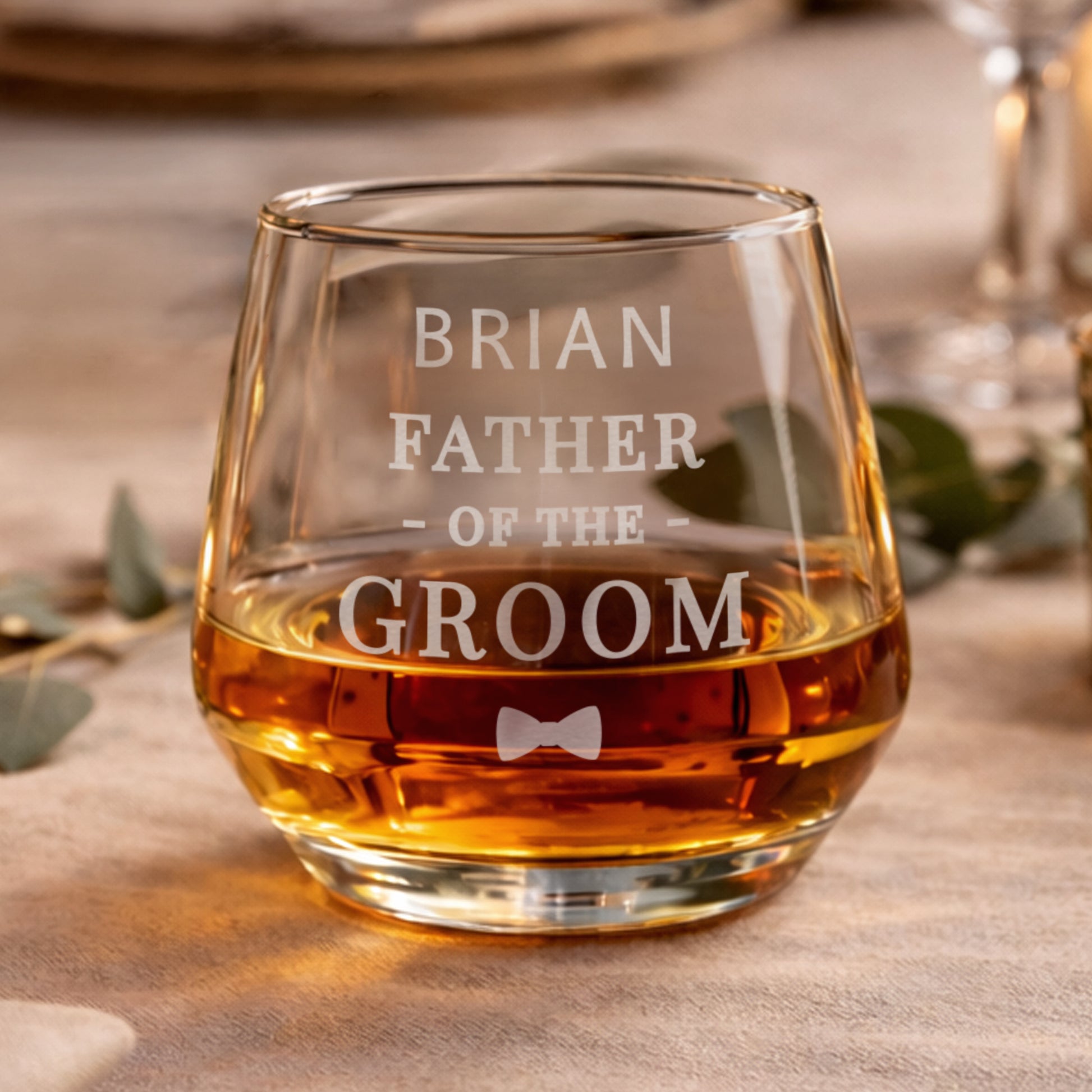 Glass filled with whiskey, engraved with 'Brian Father of the Groom' text, on a wooden surface.