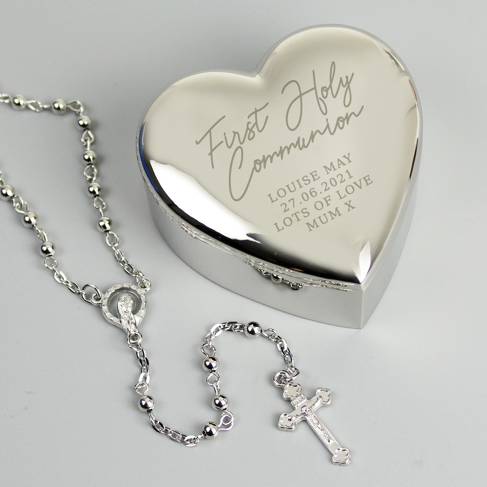 Heart-shaped silver box with engraved text and a silver rosary on a light grey background