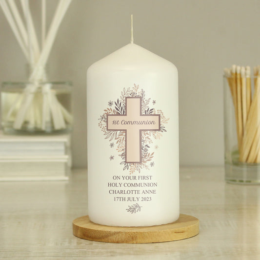 White candle with a cross design and personalised text on a wooden base, surrounded by decorative items.
