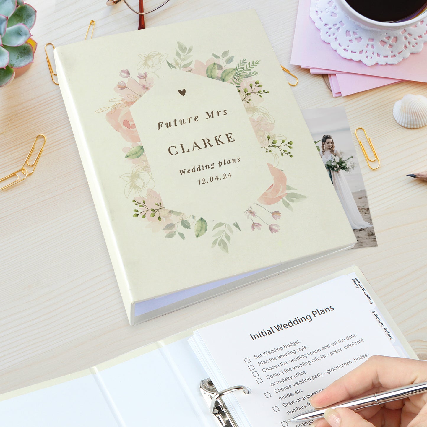 Wedding planning notebook with floral design and 'Future Mrs Clarke' text on a desk with stationery items.