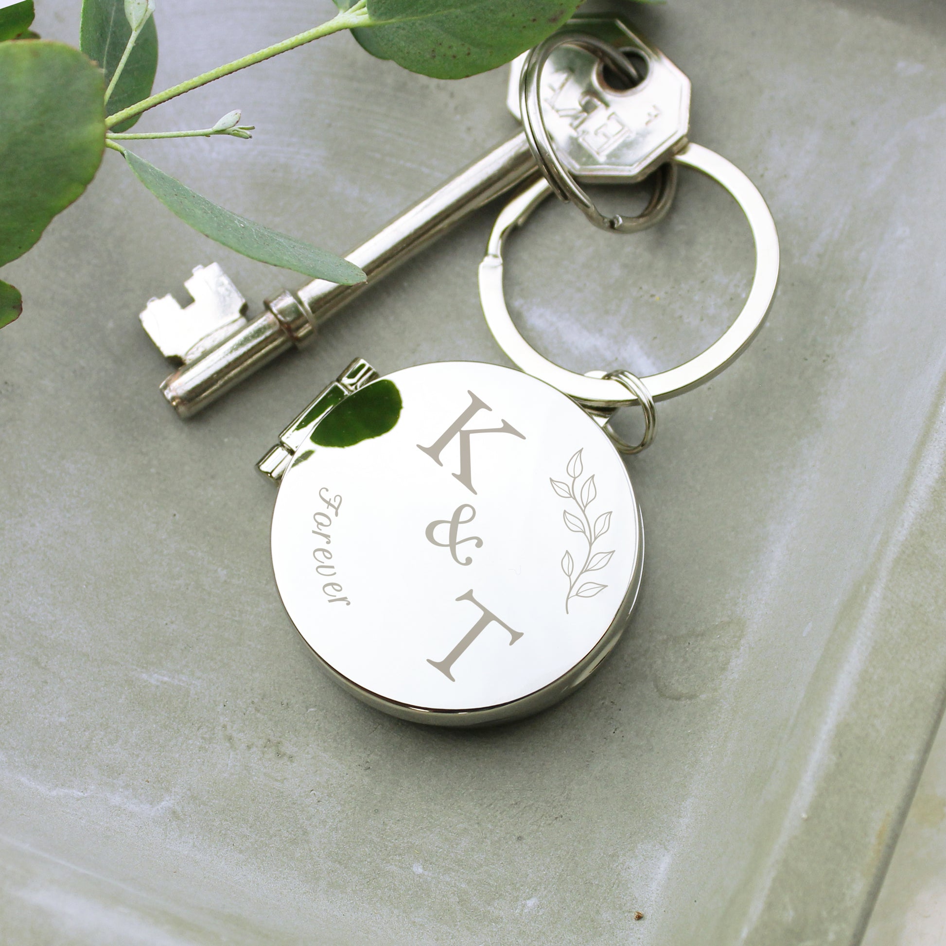 Silver keychain with engraved initials on a light green surface with leaves.
