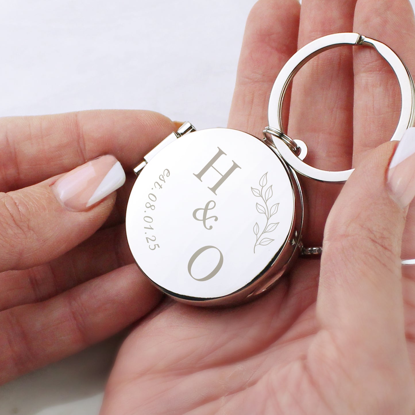 Silver keychain with engraved initials 'H & O' held by a hand on a light background