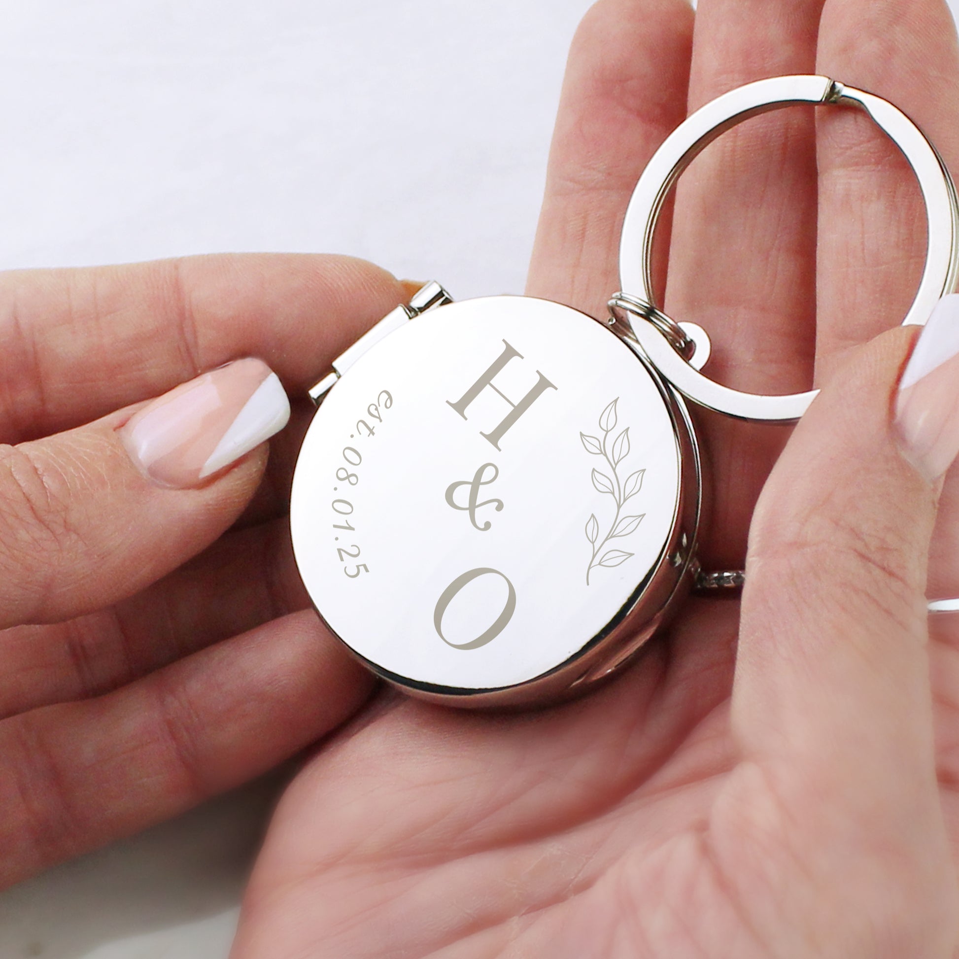 Silver keychain with engraved initials 'H & O' held by a hand on a light background