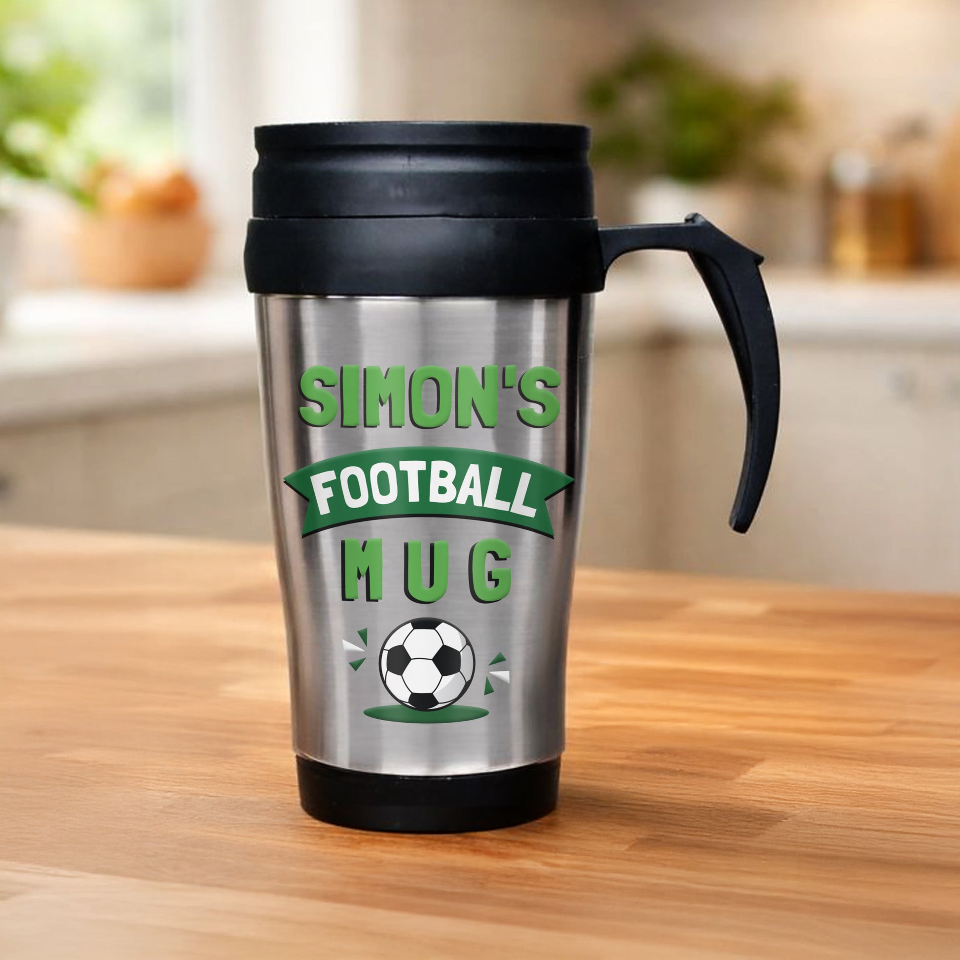 Silver mug with black handle and lid, featuring 'Simon's Football Mug' text and design on a wooden surface.