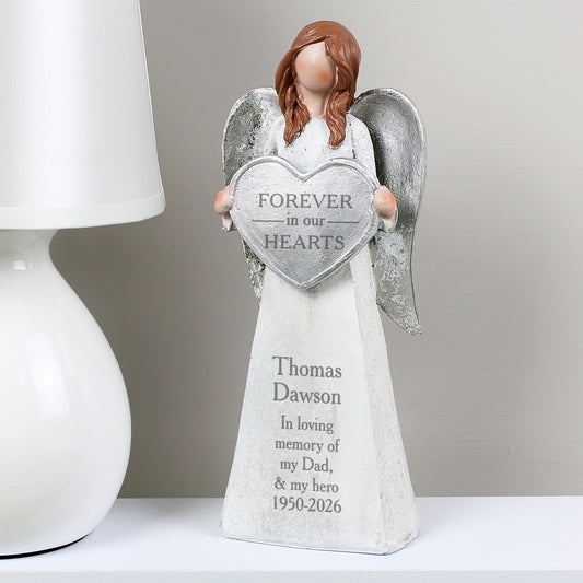 Angel figurine holding a heart-shaped plaque with engraved text on a white surface.