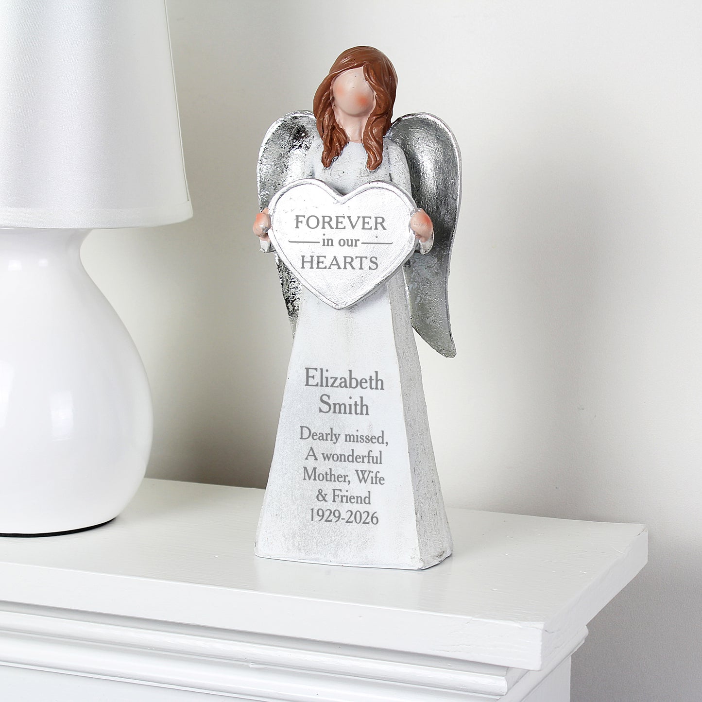 Memorial angel statue holding a heart with engraved text on a white surface.