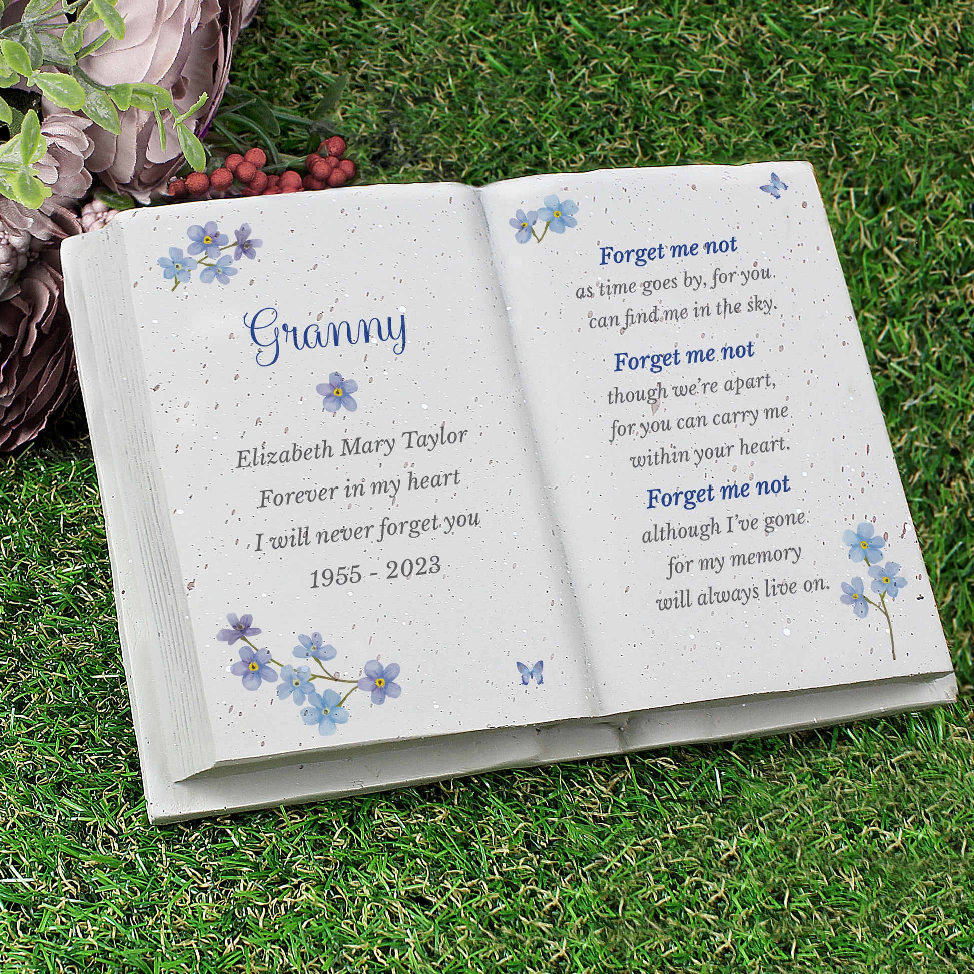 Open book with engraved text on grass, featuring floral designs and a poem.