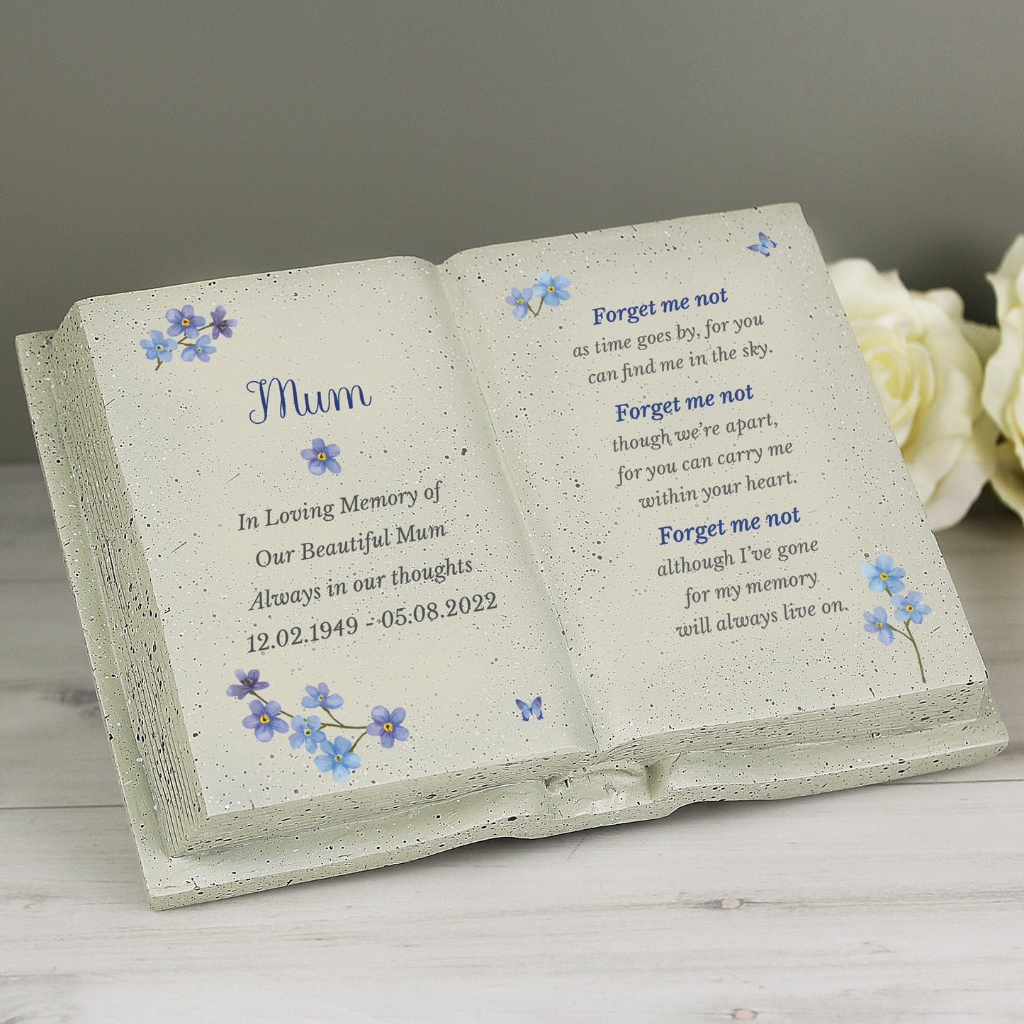 Memorial book with engraved text and forget-me-not designs on a wooden surface.