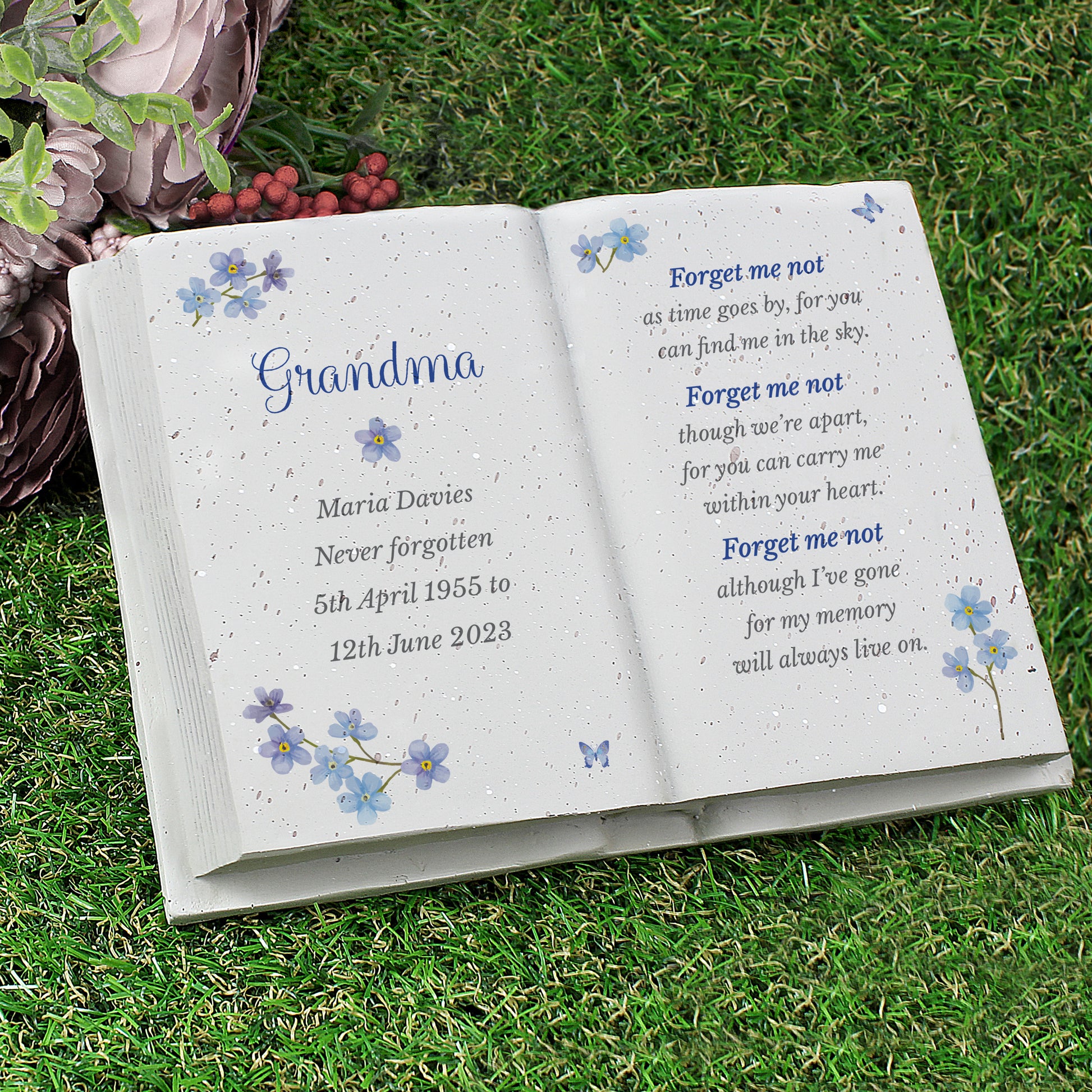 Open book with engraved text on grass, featuring floral designs and a poem.