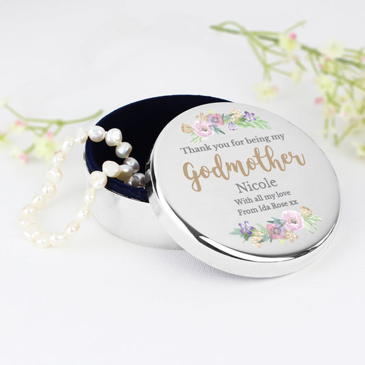Round silver container with floral design and pearl necklace on a white background