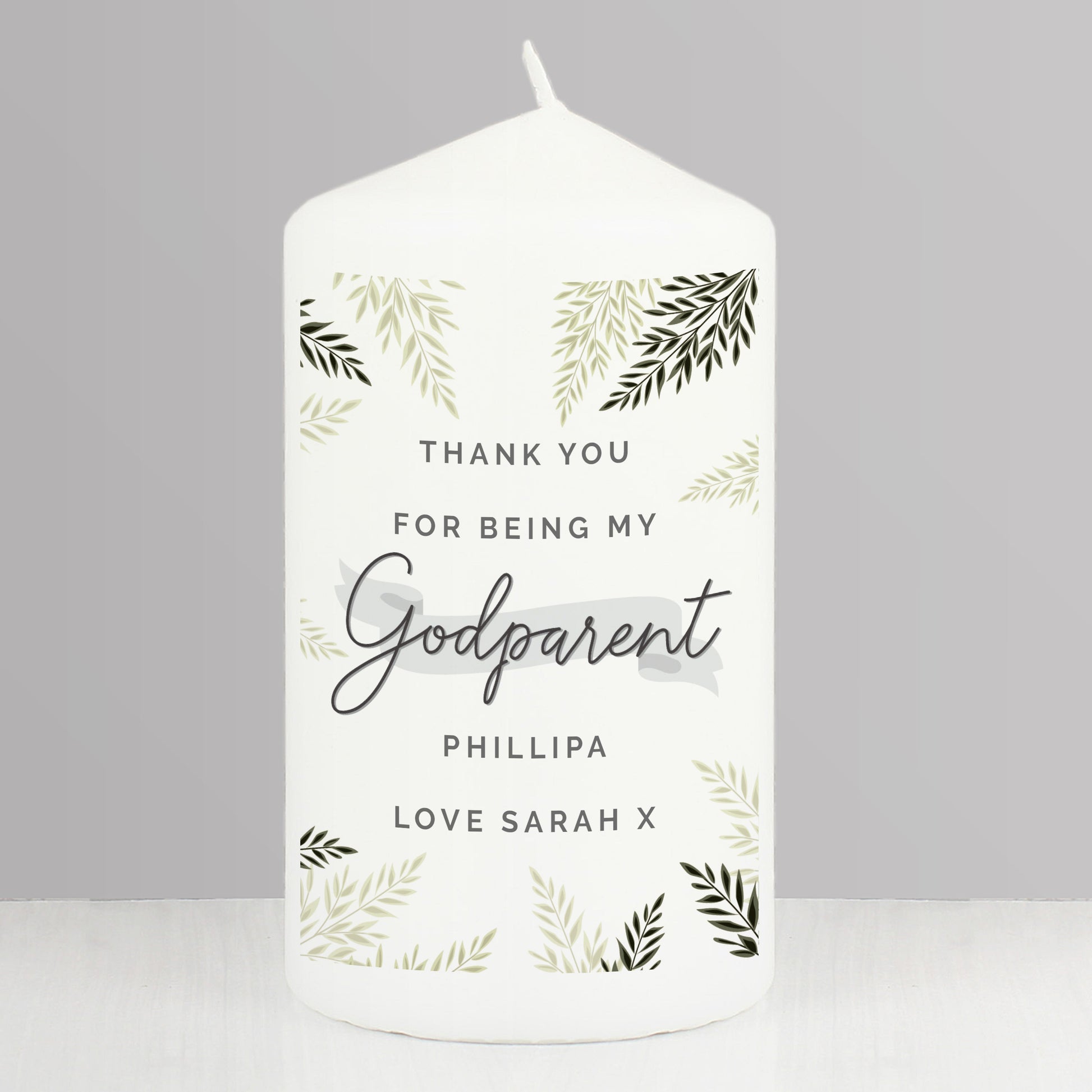 White candle with personalised text and leaf patterns on a grey background