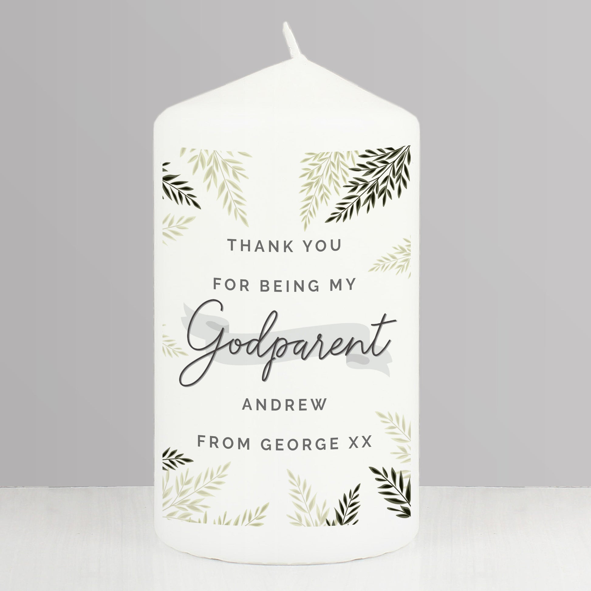 White candle with personalised text and leaf patterns on a grey background