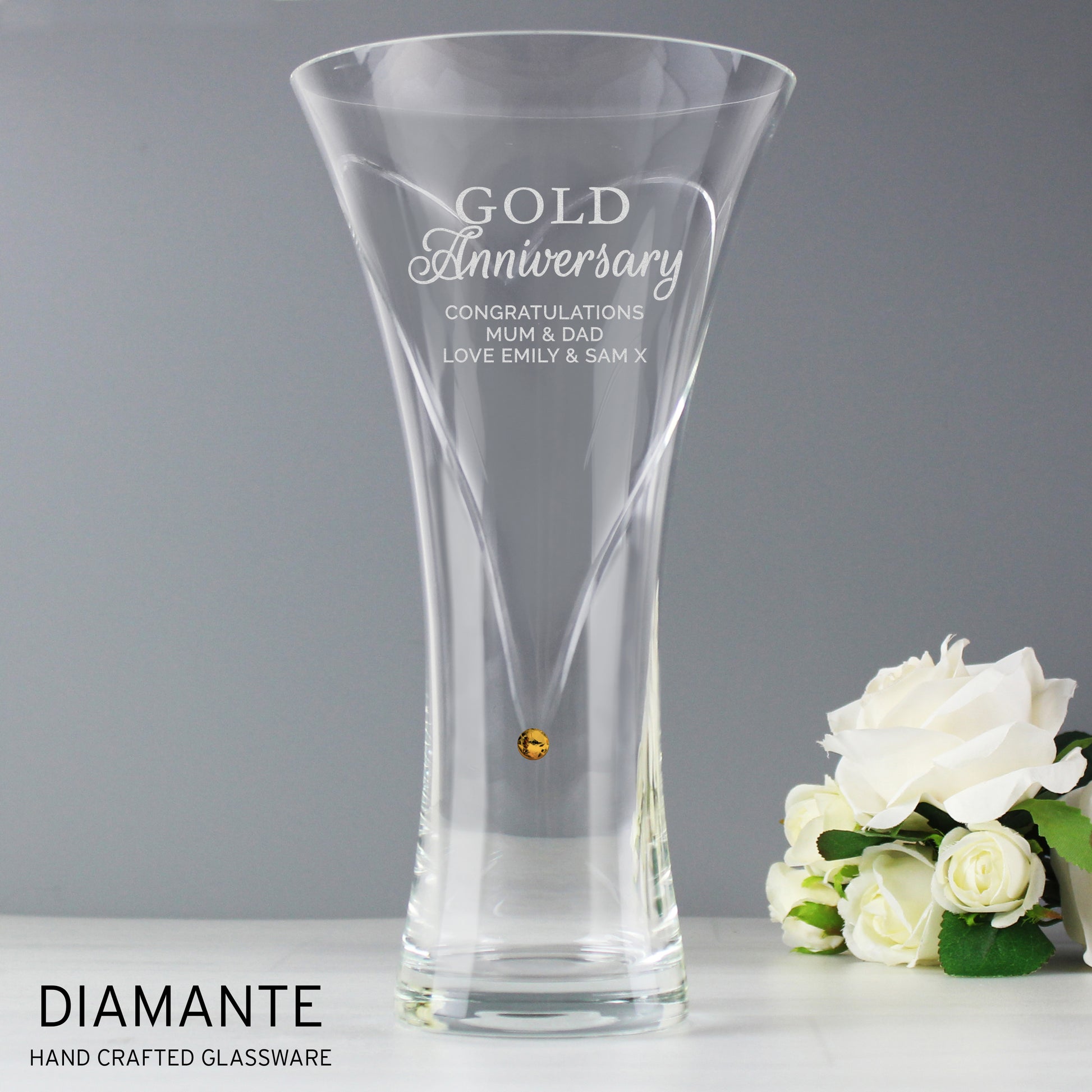 Clear glass vase with engraved text and a bouquet of white roses on a gray background
