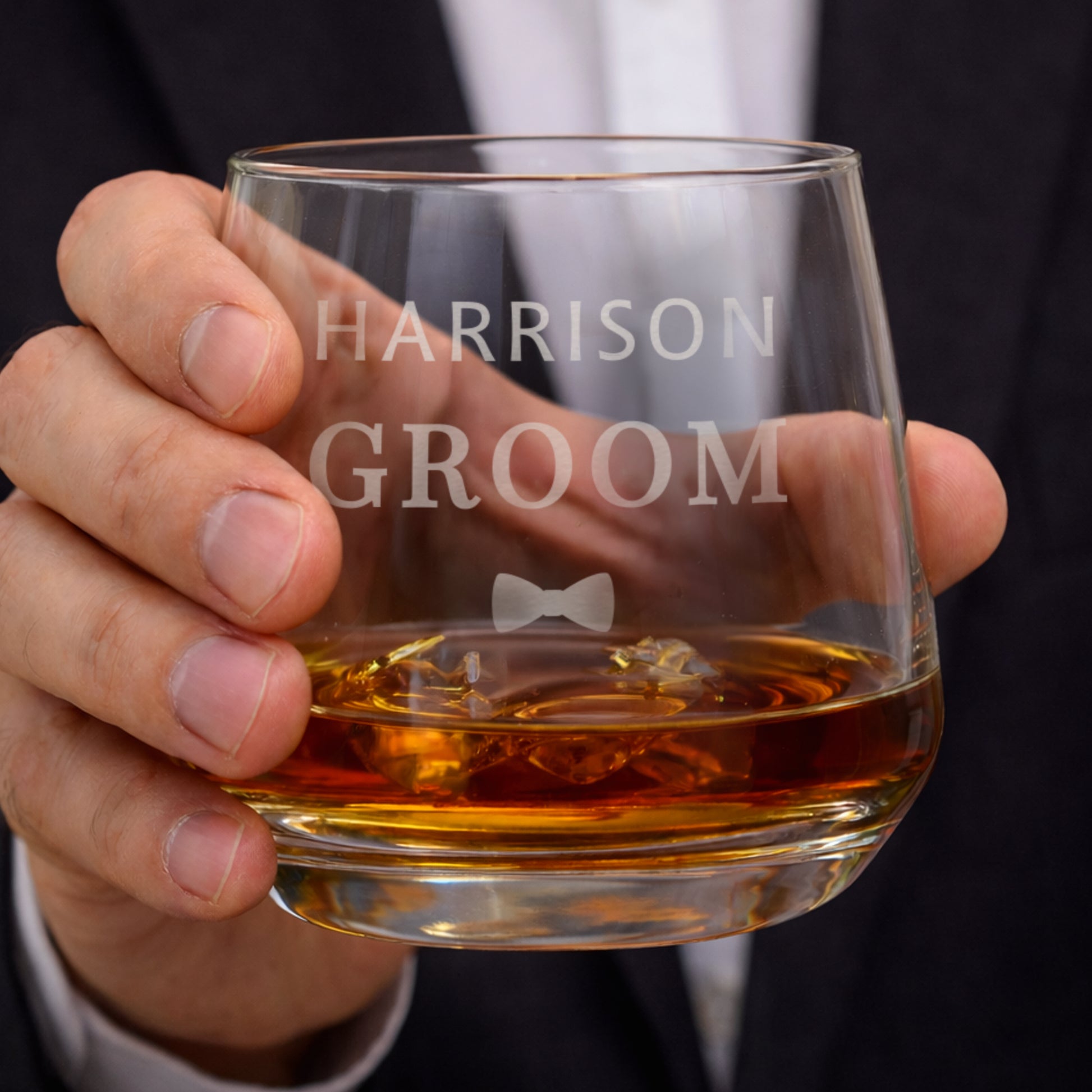 Hand holding a glass of whiskey with 'HARRISON GROOM' engraved on it.
