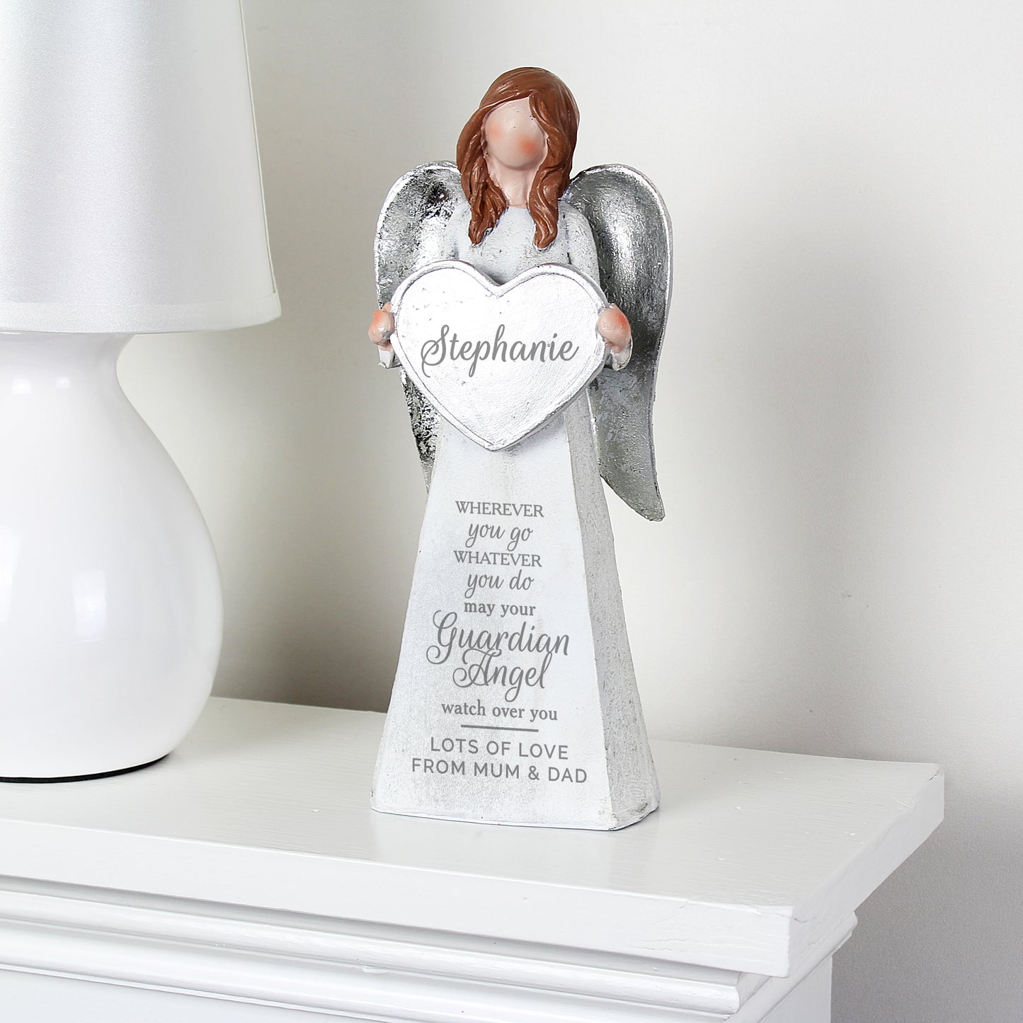 Memorial angel statue holding a heart with engraved text on a white surface.