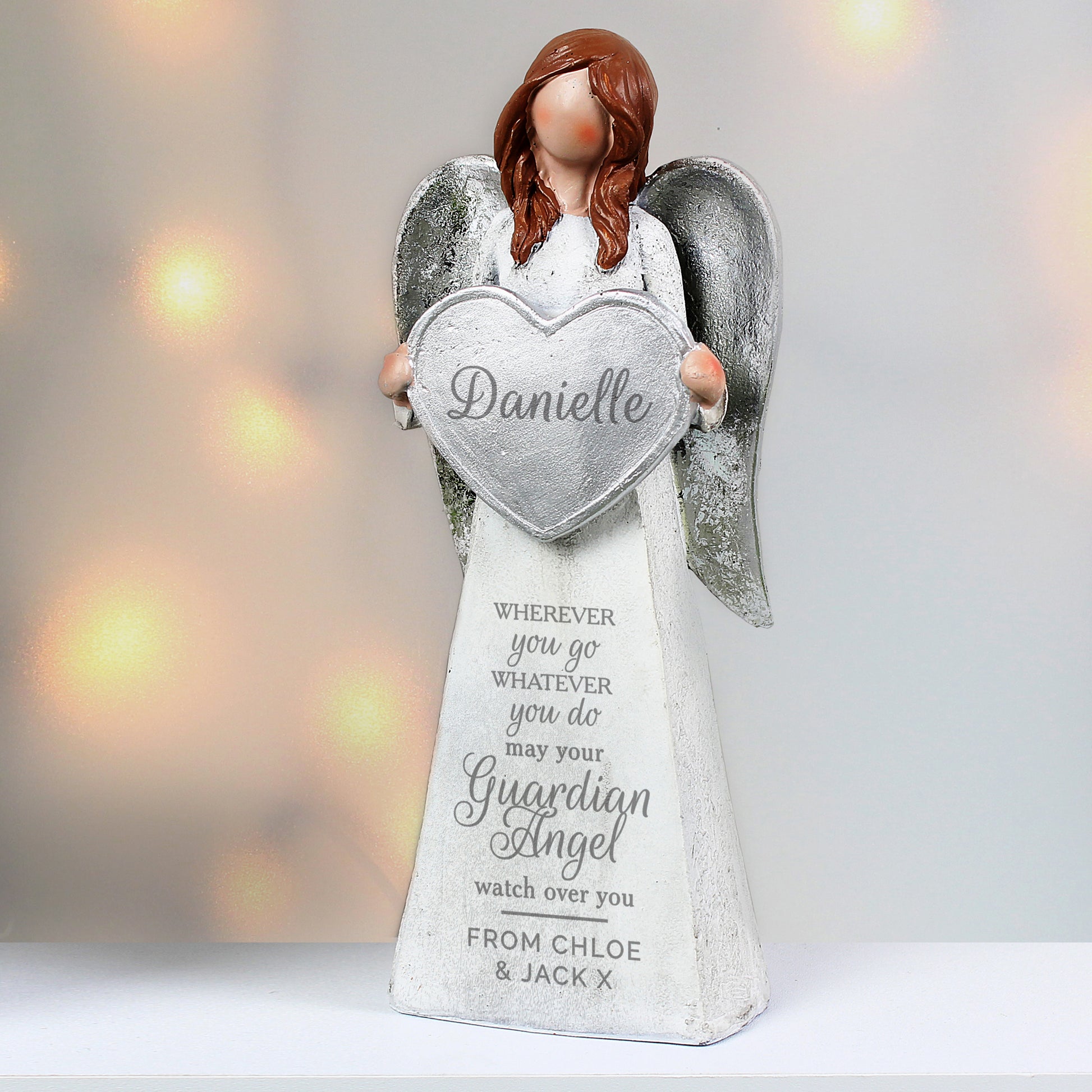 Angel figurine holding a heart-shaped 'Danielle' sign with personalised text on a blurred light background.