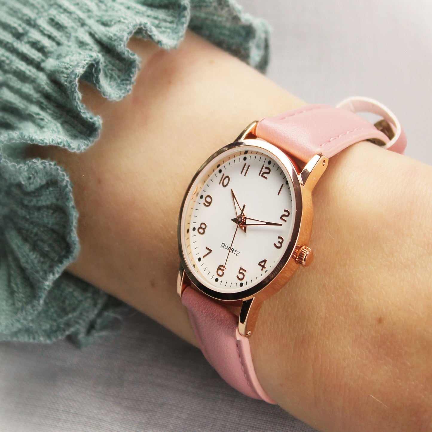 Wristwatch with a pink strap on a wrist, wearing a green textured sleeve.