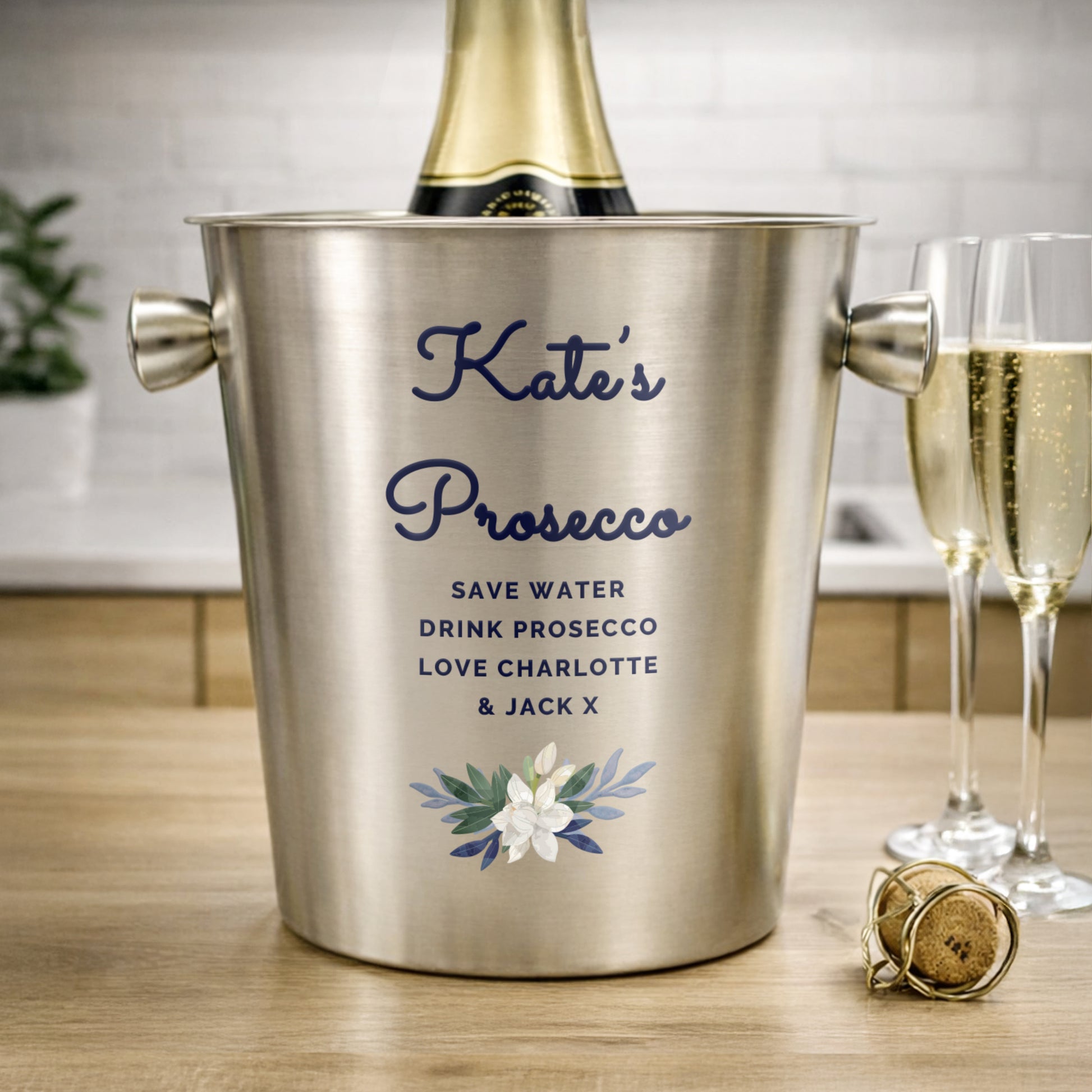 Personalised stainless steel ice bucket with Kate's Prosecco - Save Water Drink Prosecco Love Charlotte & Jack X. Showing Prosecco bottle, glasses, and cork on a wooden surface. (Not included.)