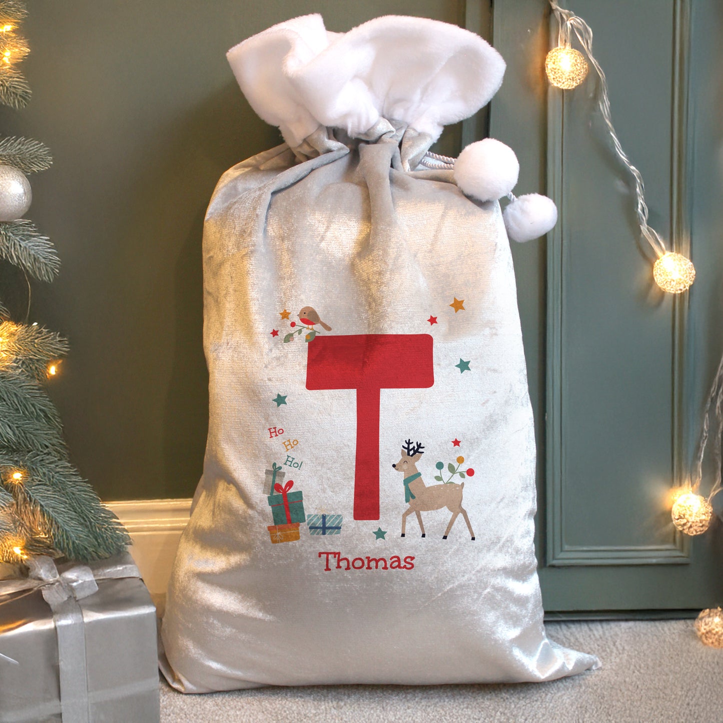 White fleece Christmas sack with an initial T and reindeer image, by a tree.