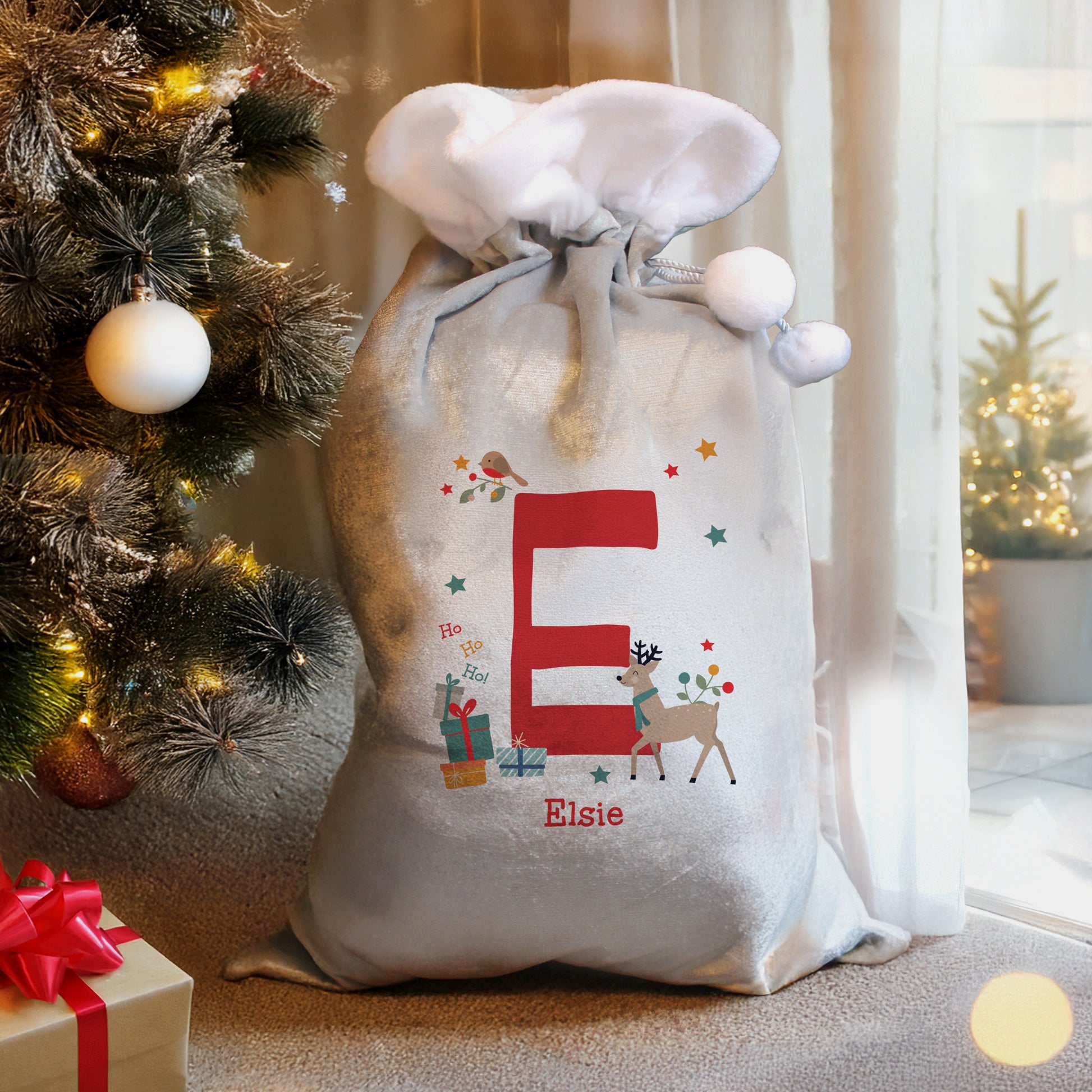 Personalised Christmas sack with 'E' and 'Elise' text, next to a decorated Christmas tree.