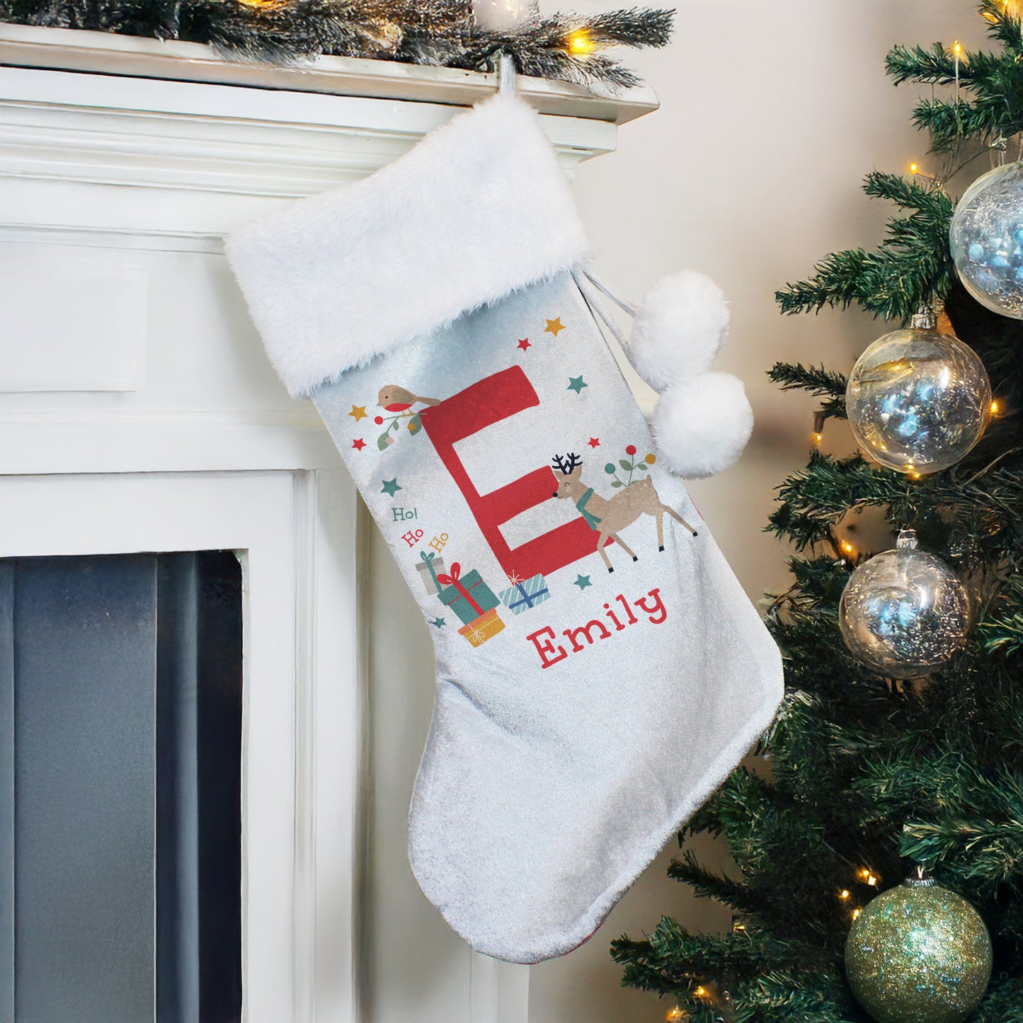 Personalised Christmas stocking with 'E' and 'Emily' text, hanging by a fireplace with a decorated tree.