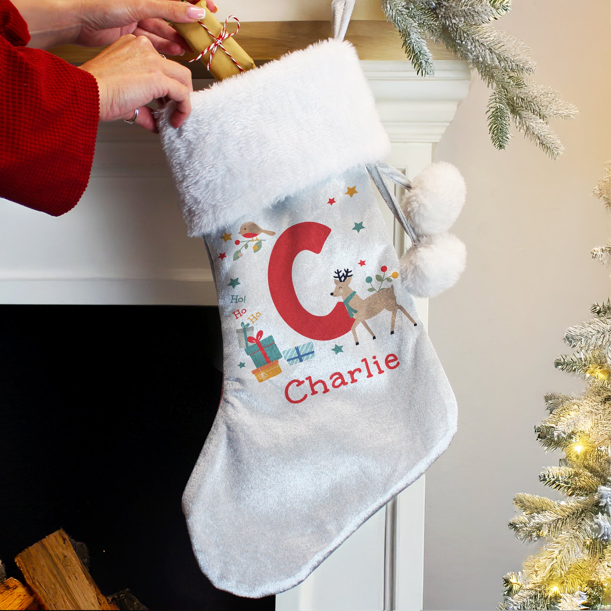 Personalised Christmas stocking with 'C' and 'Charlie' text, held by a person in a red sleeve, against a festive background.
