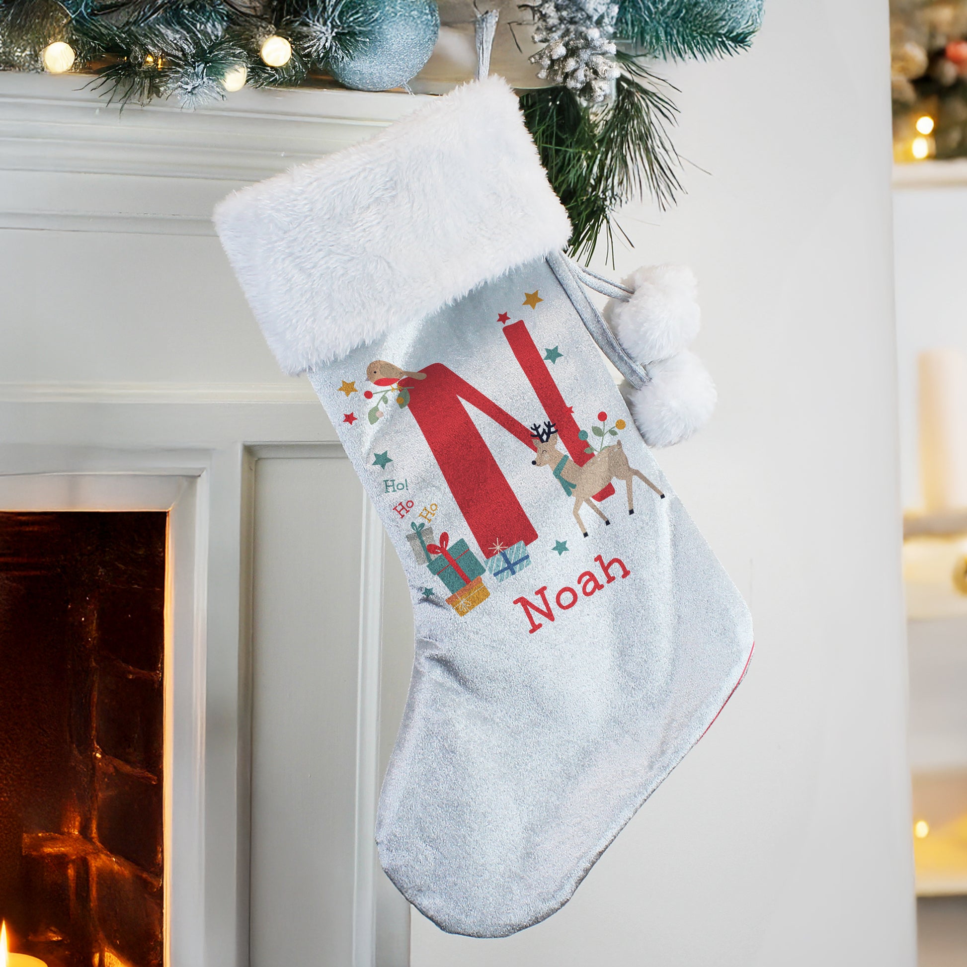 Personalised Christmas stocking with 'N' and reindeer design, hanging by a fireplace.