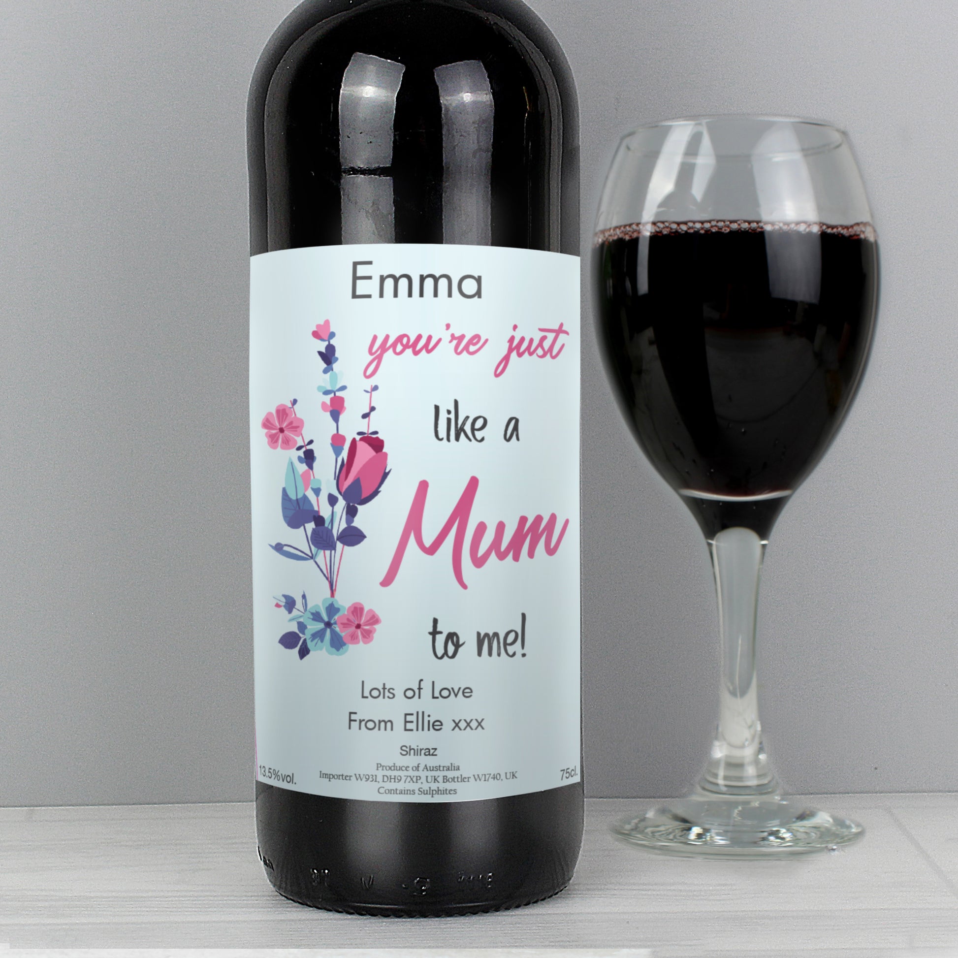 Wine bottle with a personalised label next to a glass of red wine on a grey background
