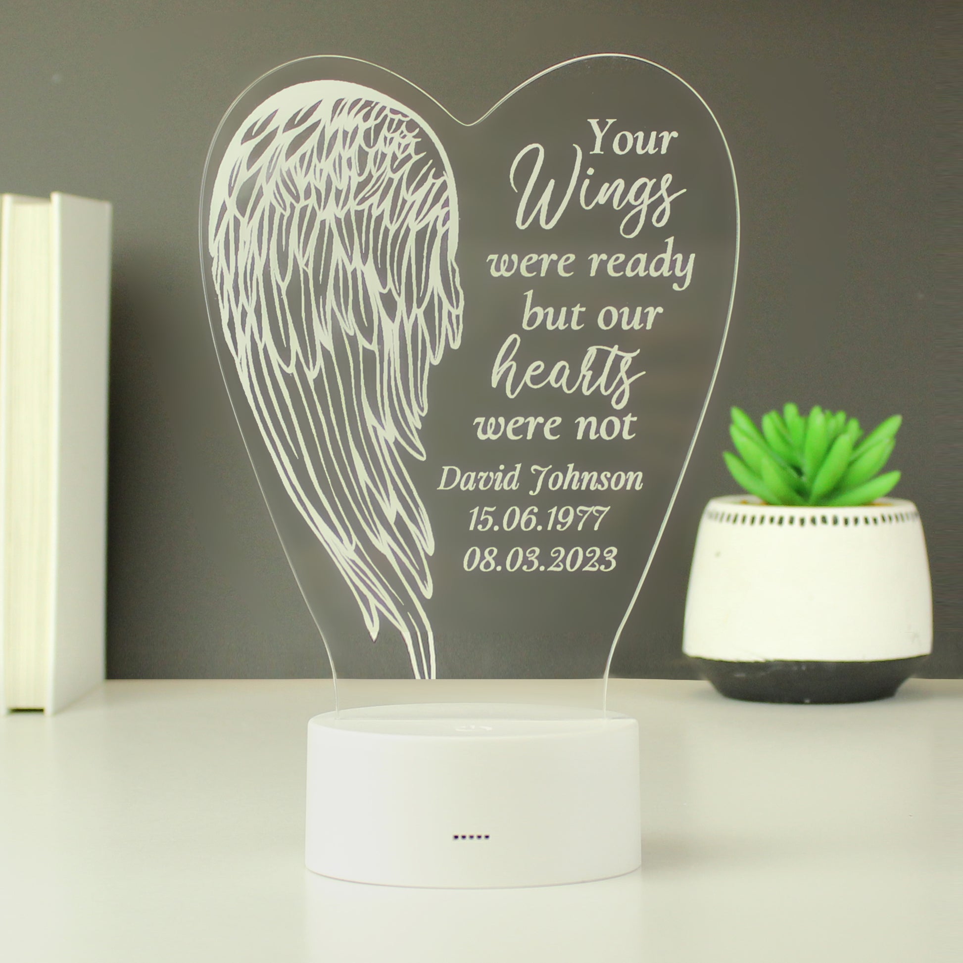 Heart-shaped plaque with angel wing design and engraved text on a white surface.