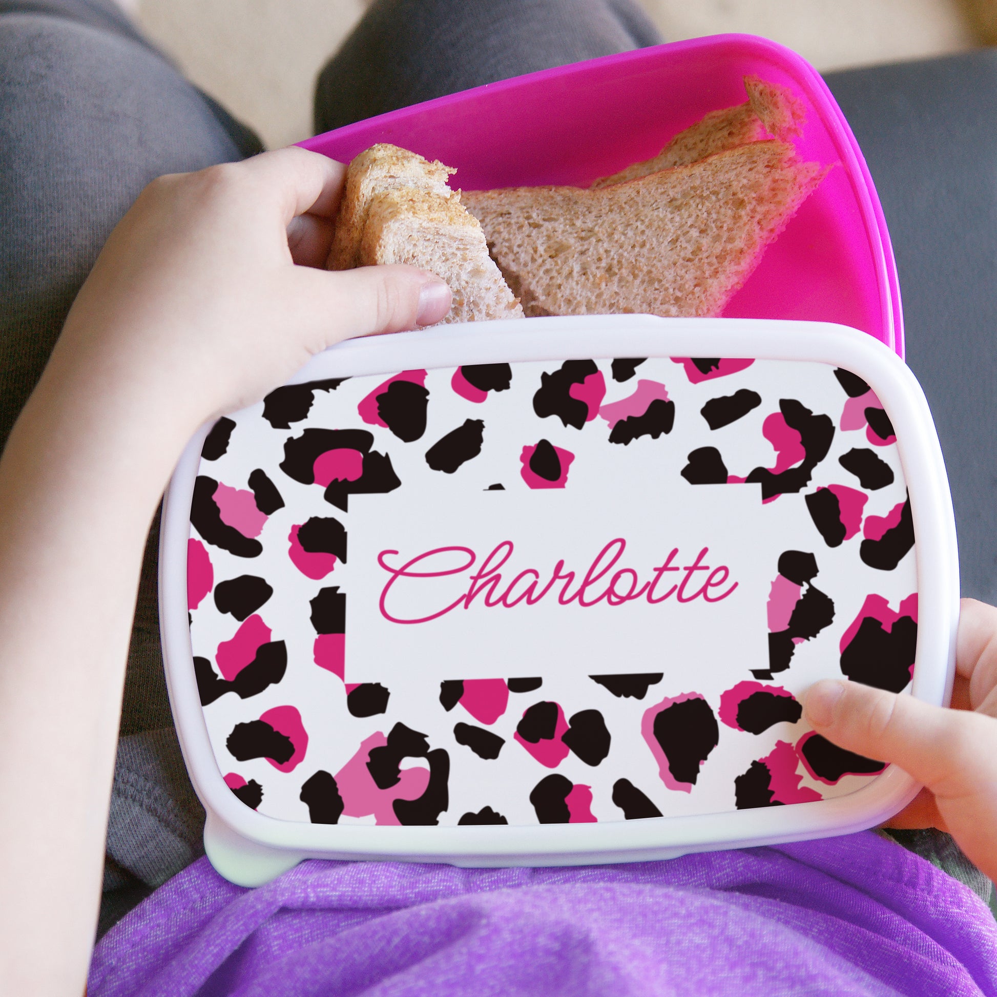 Leopard print lunch box with 'Charlotte' on it, held by a person.