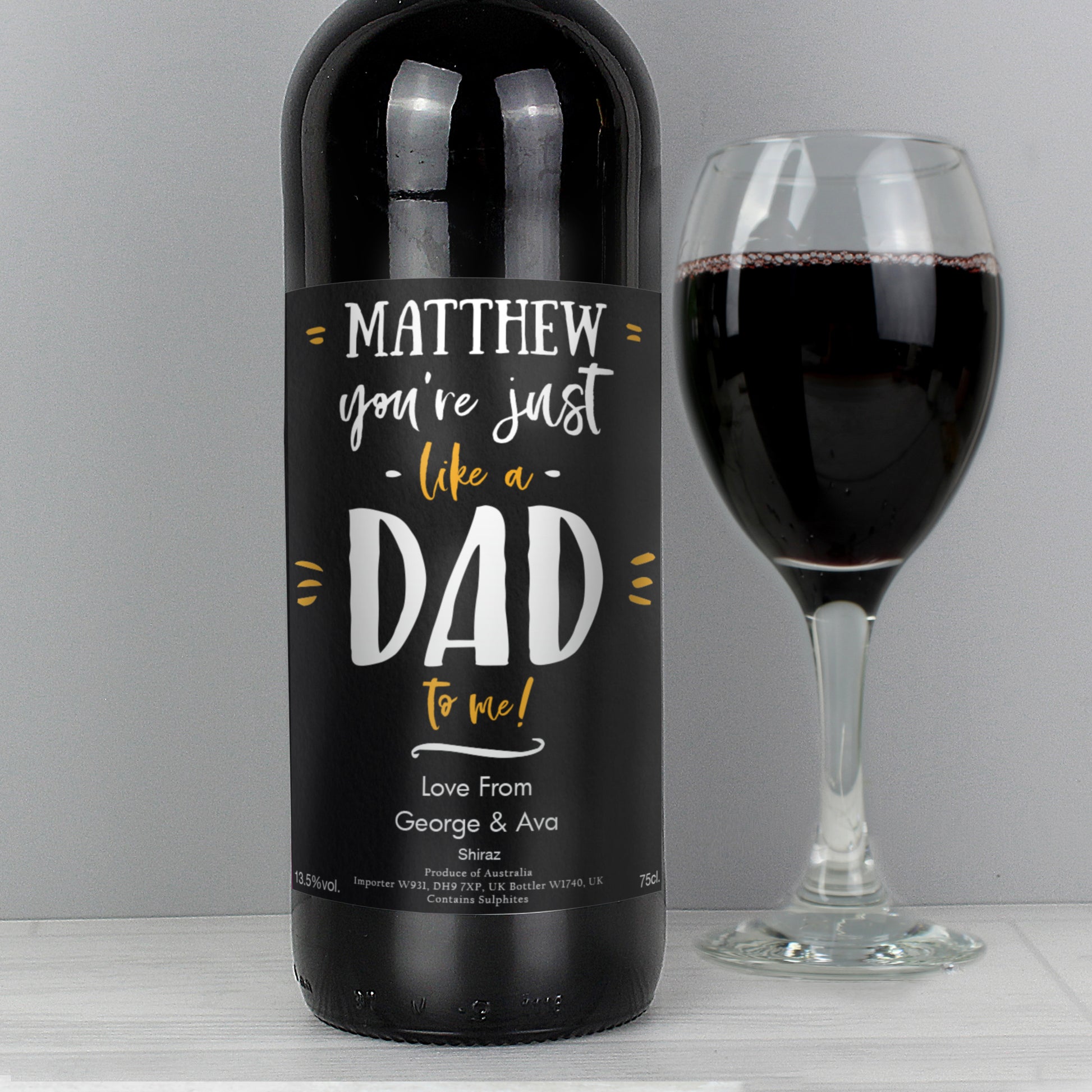 Wine bottle with a personalised label next to a glass of red wine on a grey background