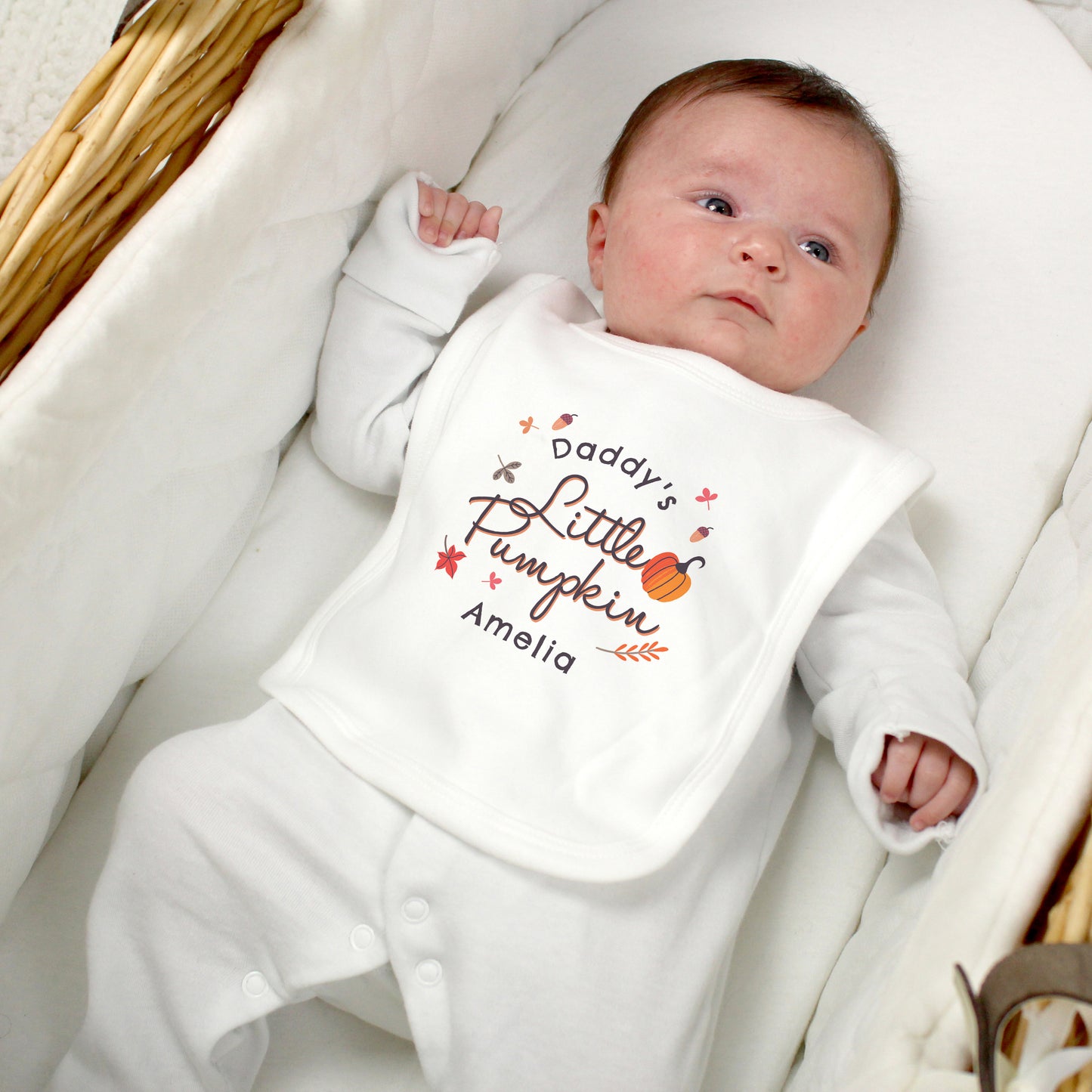 Newborn baby wearing a bib with 'Daddy's Little Pumpkin Amelia' text, lying on a white blanket.